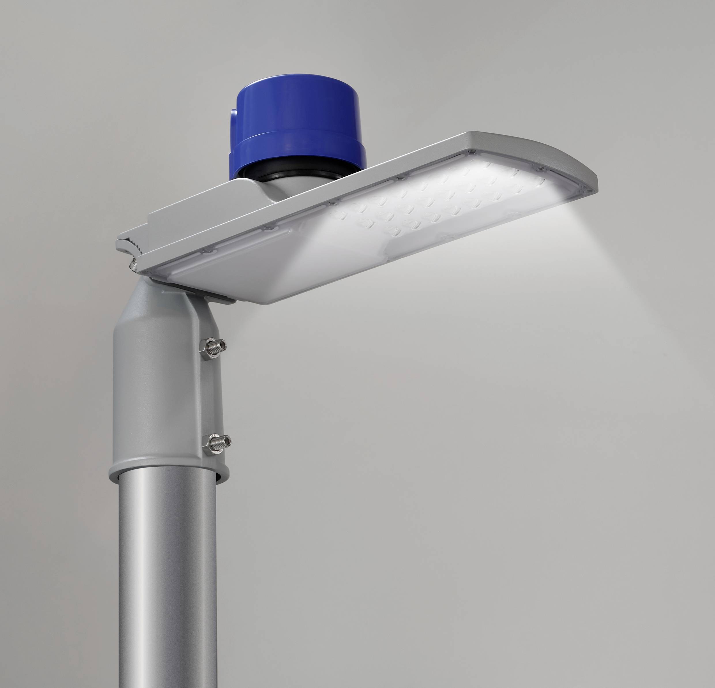 Eine moderne, silberfarbene LED-Straßenlaterne mit blauem Sensor oben, die in einem hellen Innenraum montiert ist und Licht nach unten strahlt.