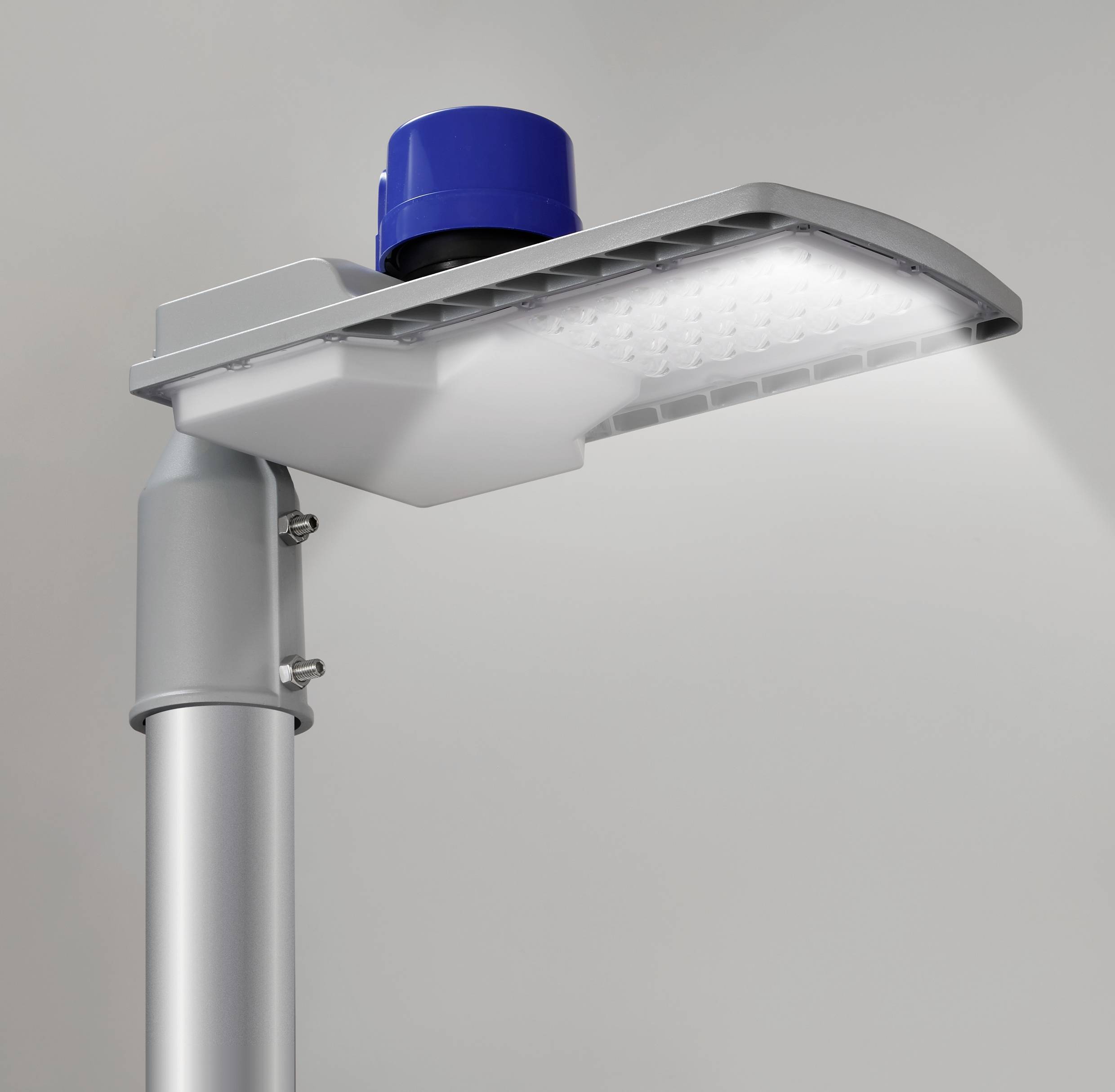 Eine moderne LED-Straßenlaterne mit blauem Sensor oben, leuchtet hell auf grauem Hintergrund.