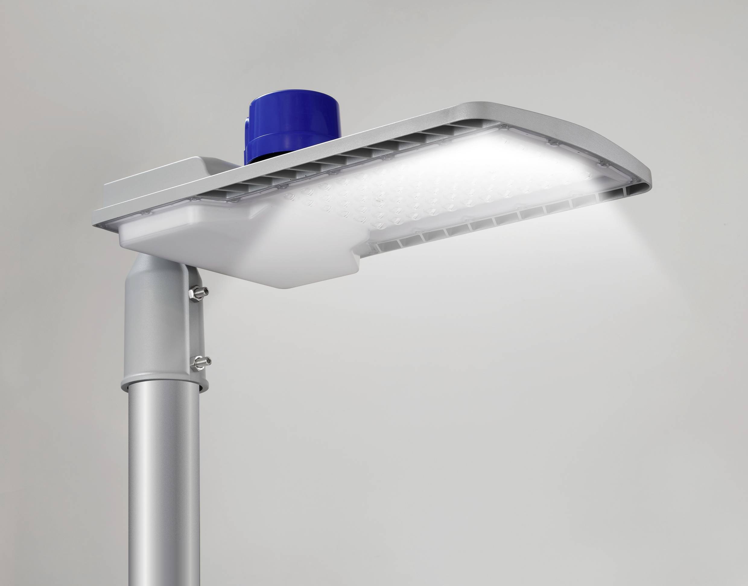 Eine moderne LED-Straßenlampe leuchtet hell. Sie ist an einem grauen Metallmast befestigt, mit einem blauen Aufsatz oben.