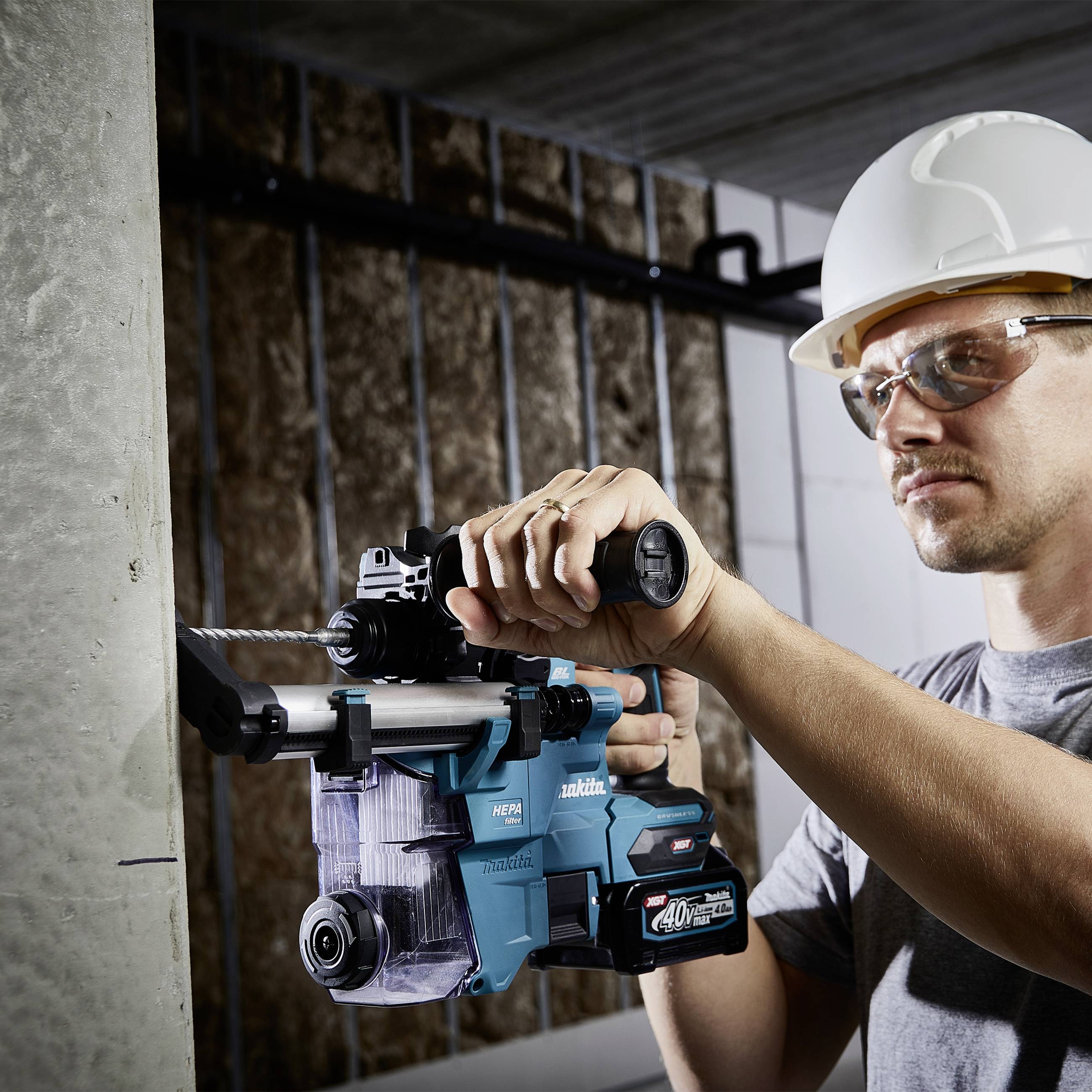 Ein Bauarbeiter mit Schutzhelm und -brille benutzt ein Elektrowerkzeug, um in eine Betonwand zu bohren.