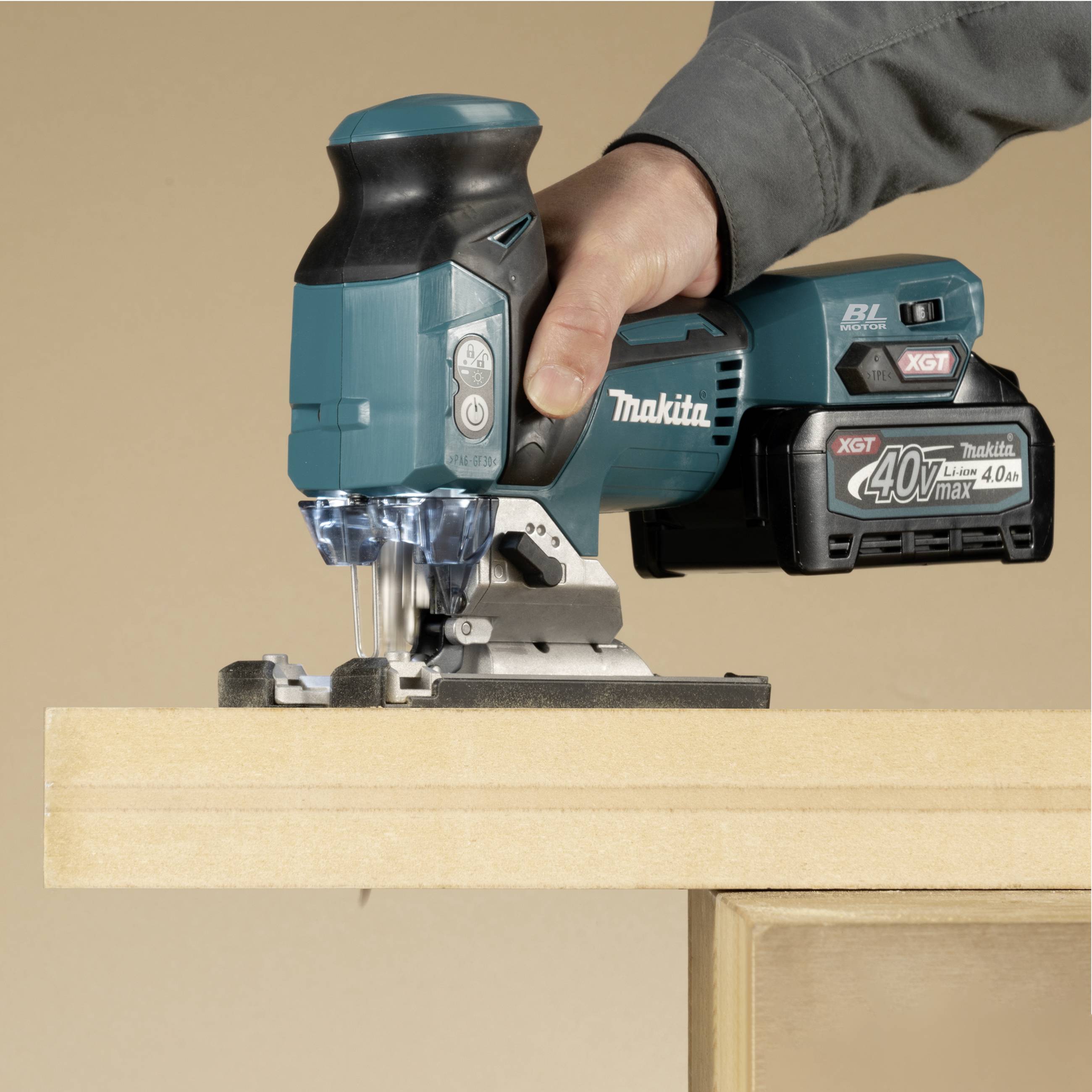 Person arbeitet mit einer blauen elektrischen Stichsäge auf einem Holzbrett. Die Stichsäge ist von der Marke Makita.
