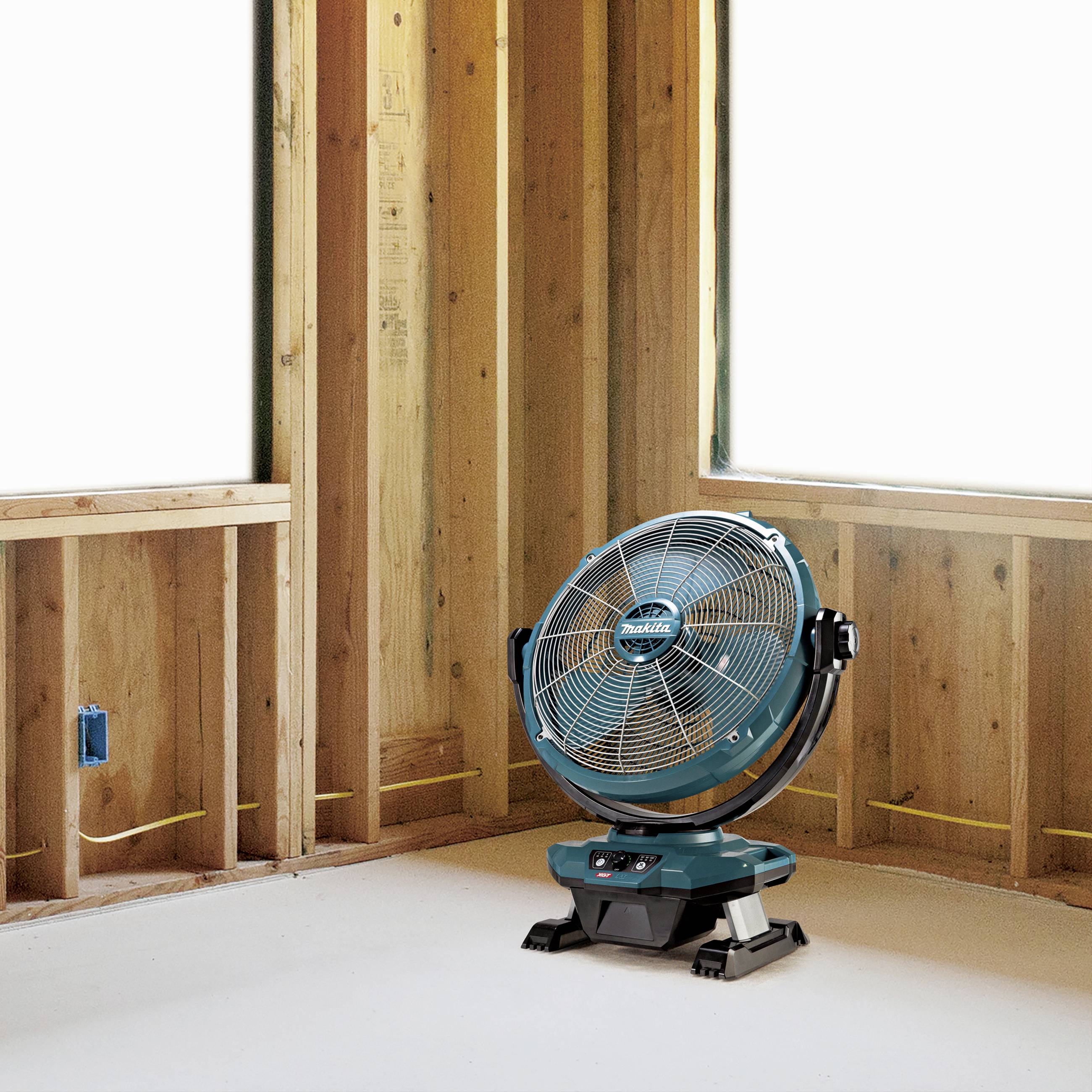 Bauzone mit sichtbaren Holzrahmen, Kabeln und Steckdose. Ein blauer Ventilator steht auf dem Boden und bläst Luft in den Raum.