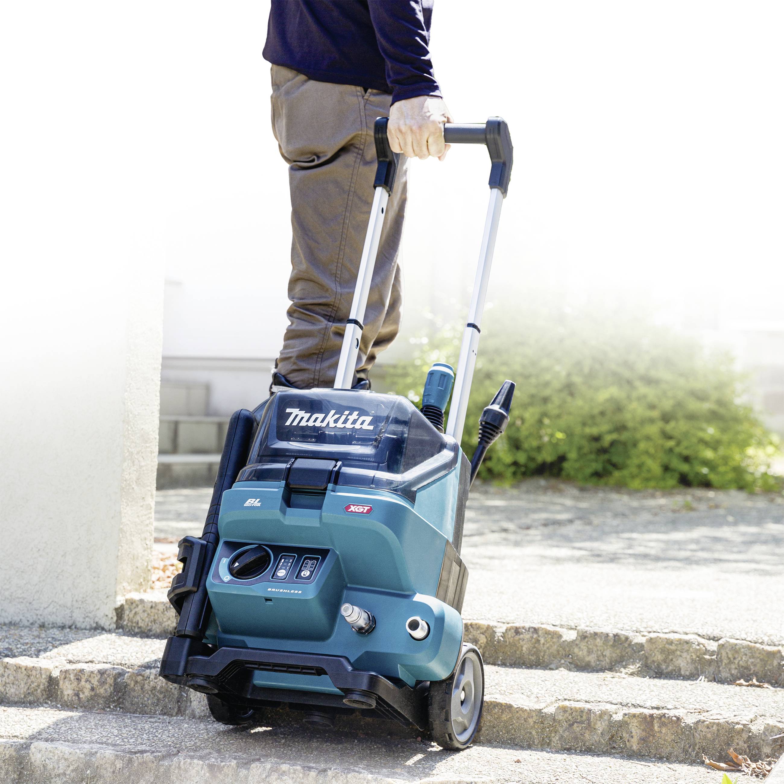 Eine Person schiebt einen tragbaren Staubsauger von Makita mit Teleskopgriff im Freien. Der Staubsauger hat zwei Räder.
