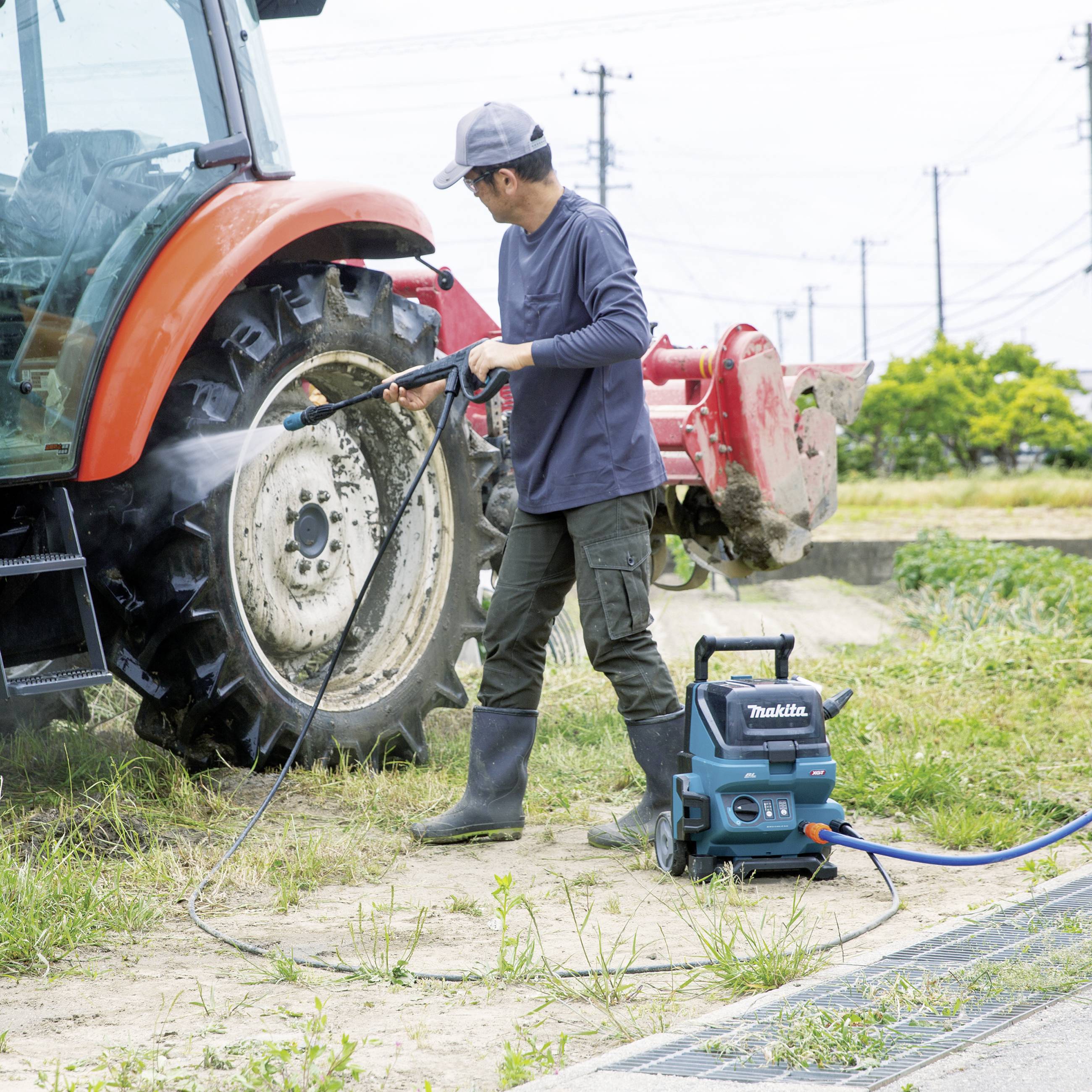 Eine Person reinigt den großen Hinterreifen eines Traktors mit einem Hochdruckreiniger auf einem Feld.