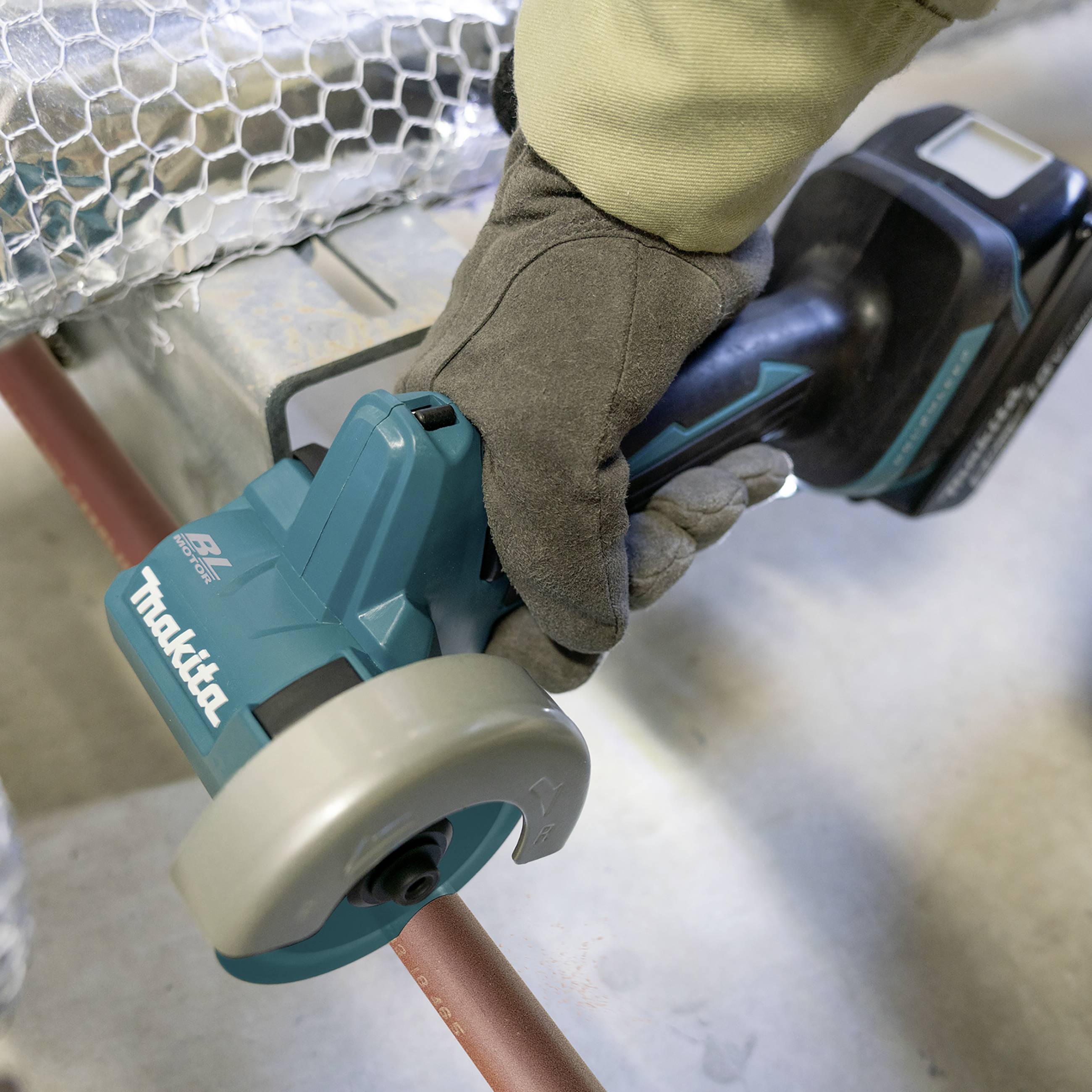 Eine Person sägt mit einer elektrischen Säge ein Kupferrohr. Die Schutzbekleidung umfasst Handschuhe. Das Werkzeug ist kabellos.