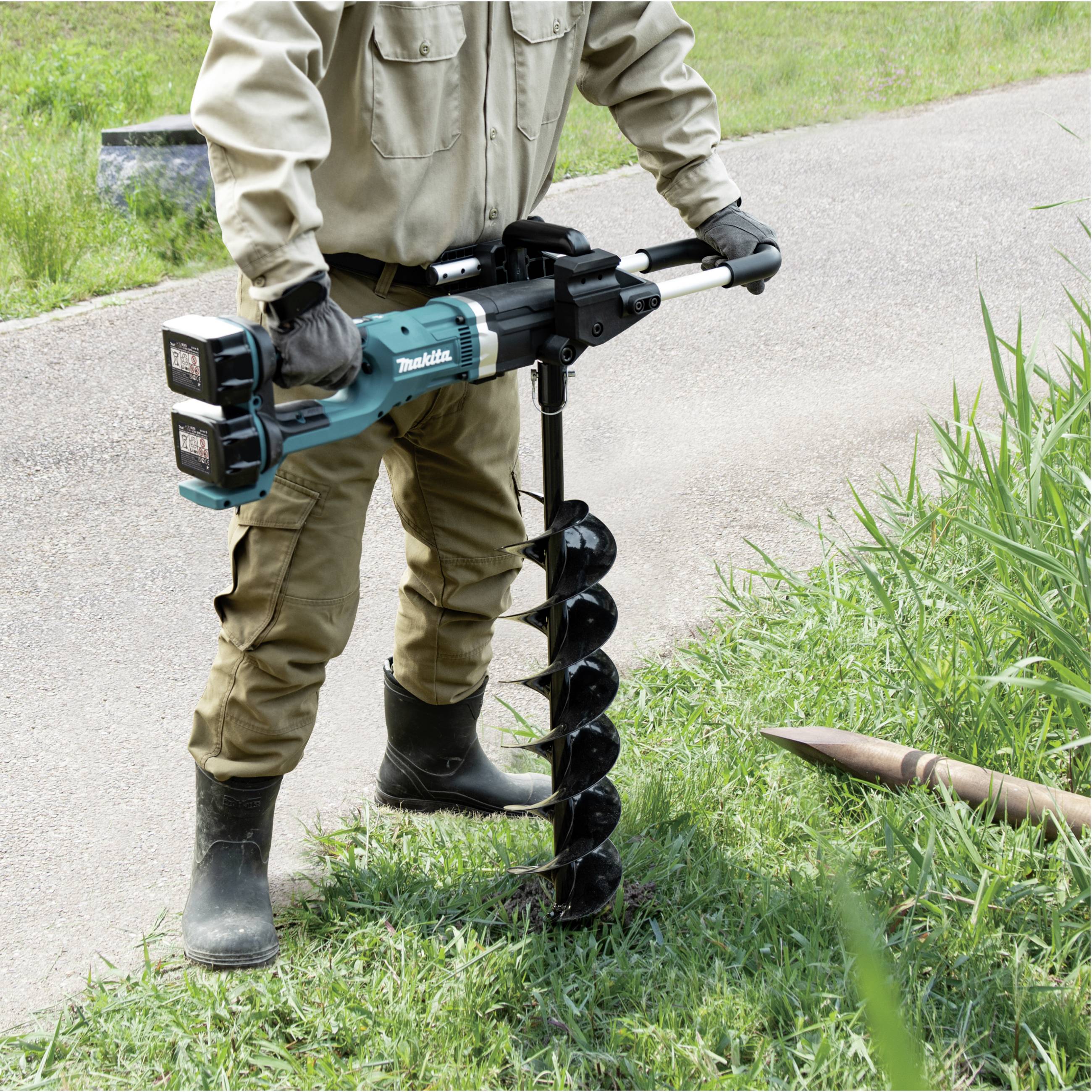 Person bohrt mit einer elektrischen Erdschnecke in den Boden neben einem Grasstück. Klarer Himmel, Fokus auf das Werkzeug.