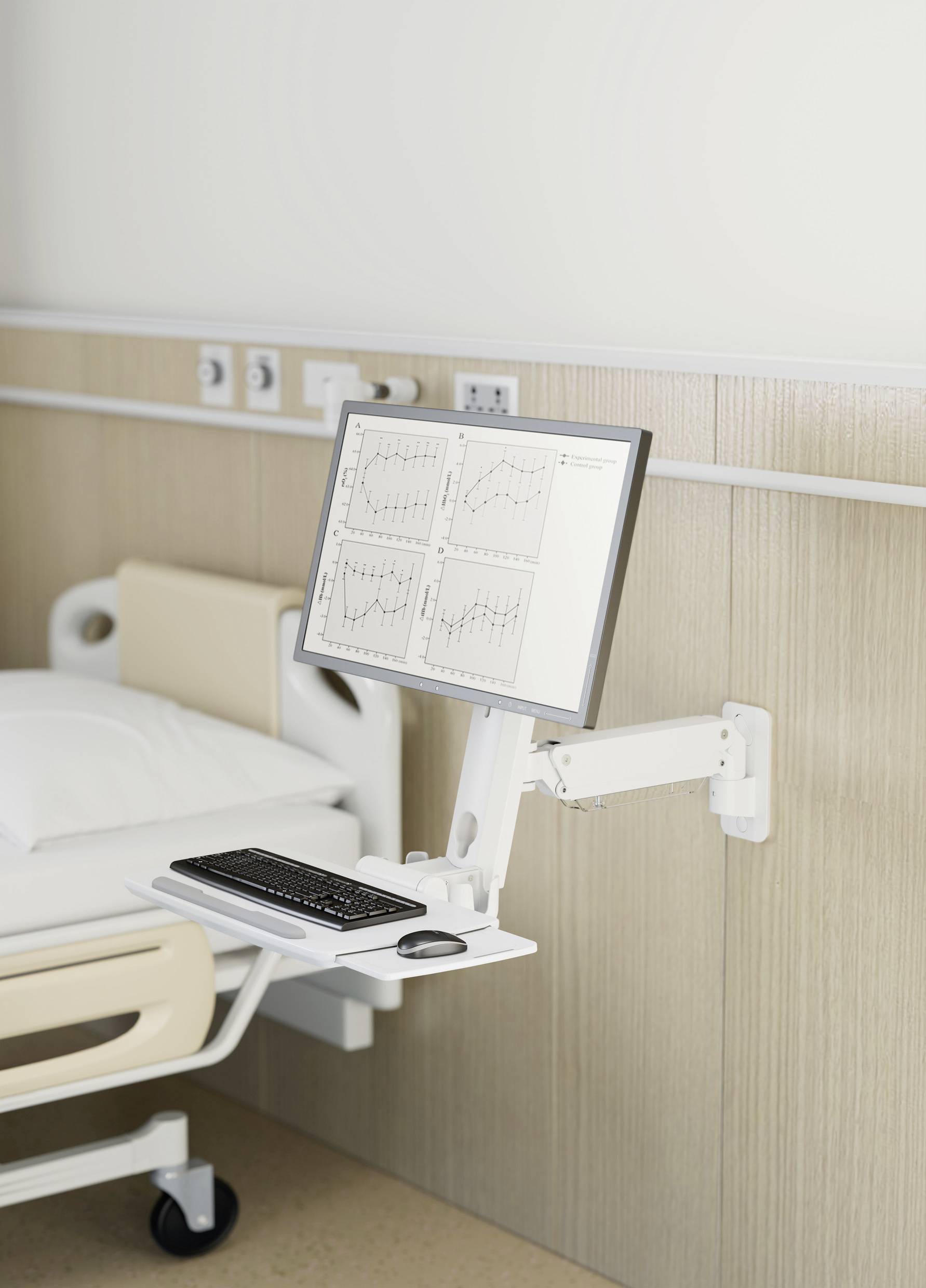 Im Krankenhaus zeigt ein Monitor an einem Krankenbett medizinische Diagramme. Daneben liegt eine Tastatur auf einem beweglichen Tisch.