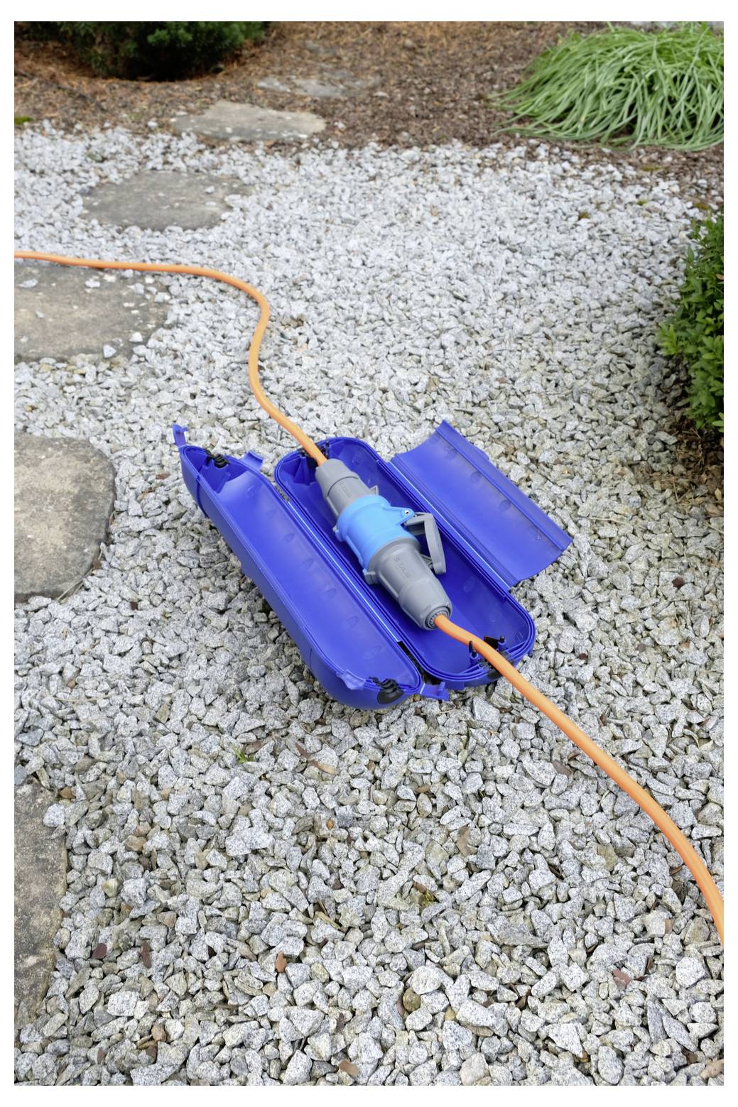 Oranger Gartenschlauch mit blauer Reparaturklemme auf einem Kiesweg verbunden, der zeigt einen geflickten Schlauchleck oder -riss.