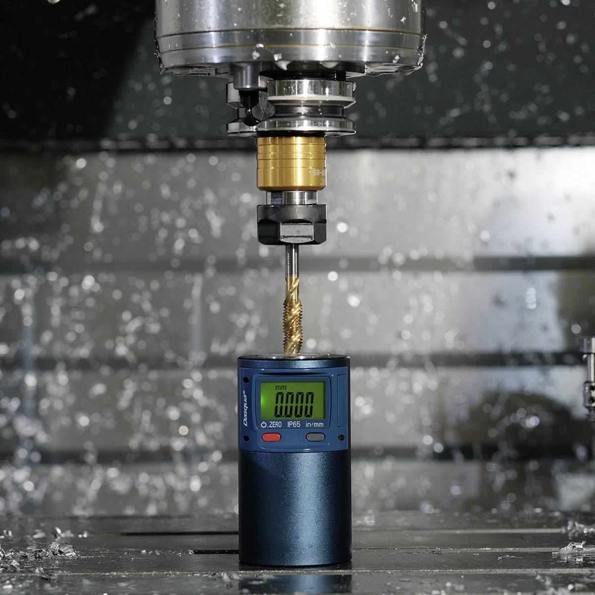 Eine Fräsmaschine bearbeitet präzise ein Metallstück, während Späne um die Maschine herumfliegen. Ein Messgerät zeigt die Drehzahl an.