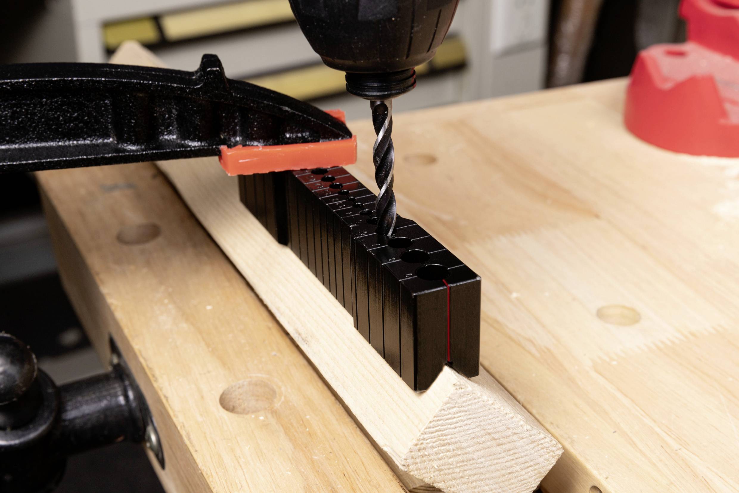 Bohrmaschine bohrt Löcher in einen Holzbalken, fixiert durch eine schwarze Klemme. Arbeitsplatz in einer Werkstatt.