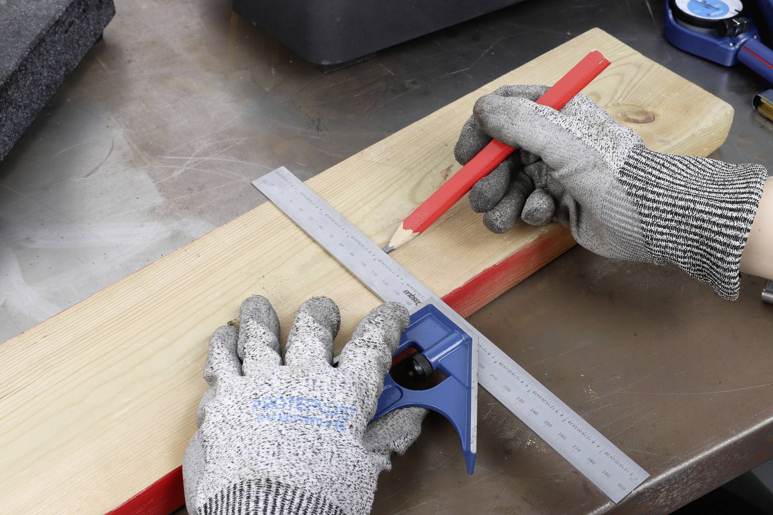 Eine Person mit grauen Handschuhen misst mit einem Winkelmesser und einem roten Bleistift auf einem Holzbrett.