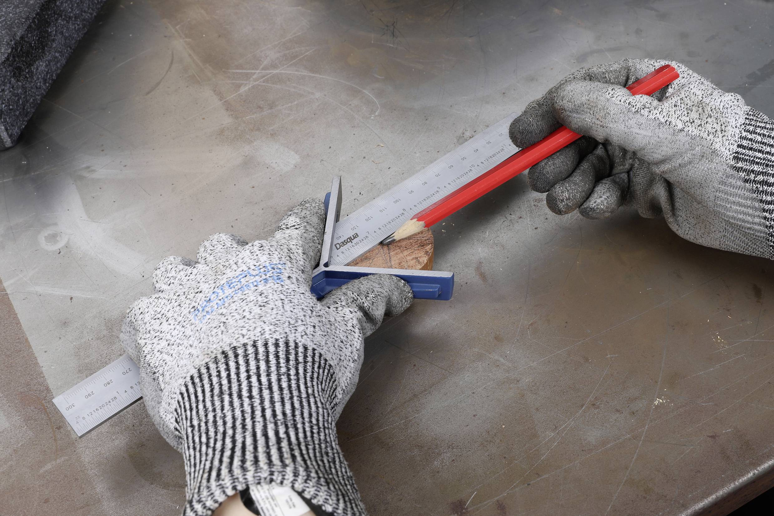 Ein Paar behandschuhter Hände misst und markiert mit einem Lineal und Bleistift auf einem Stück Holz.
