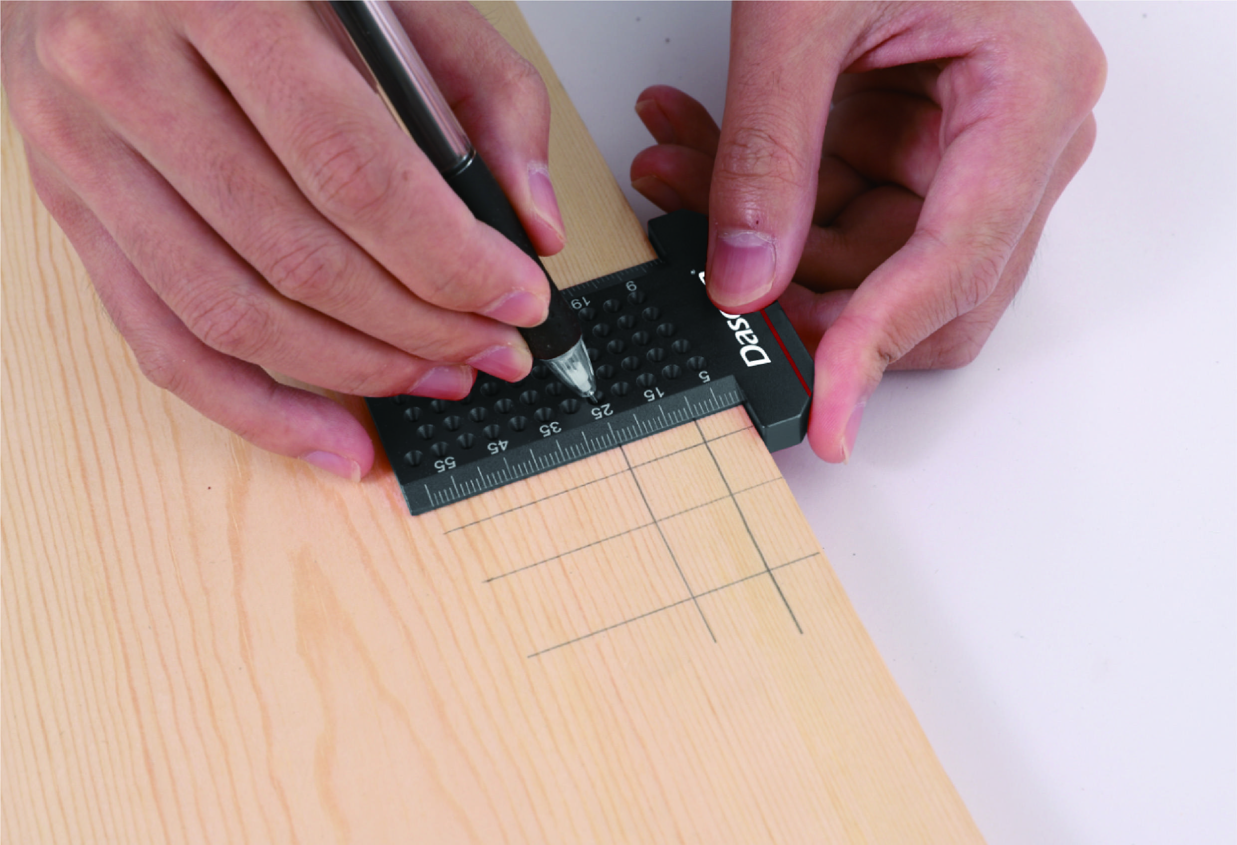 Eine Person verwendet ein Lineal und Bleistift, um präzise Linien auf einem Holzbrett zu zeichnen. Hände und Werkzeuge sind sichtbar.