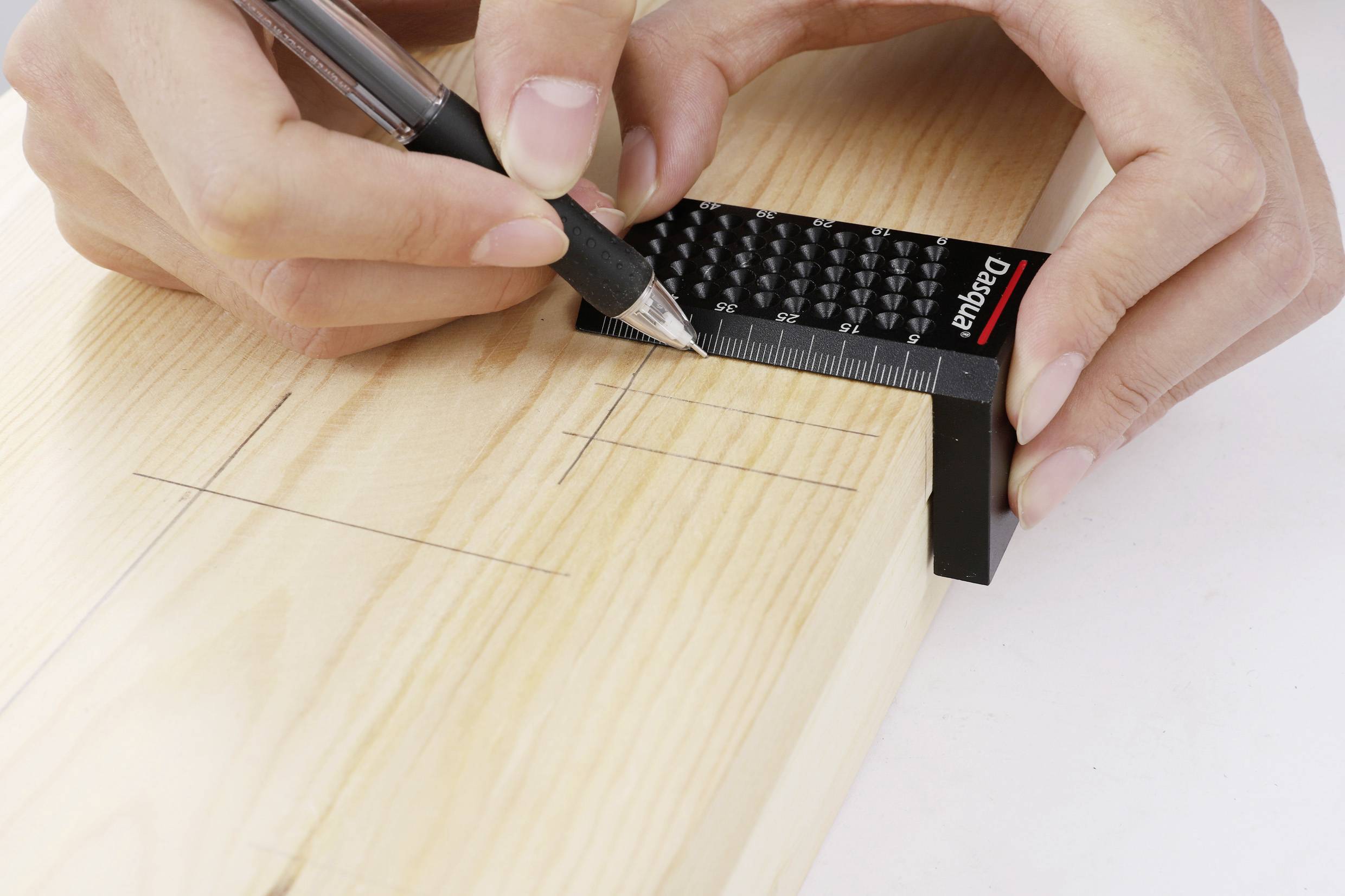 Eine Hand markiert mit Bleistift und Lineal präzise Linien auf einem Holzbrett.