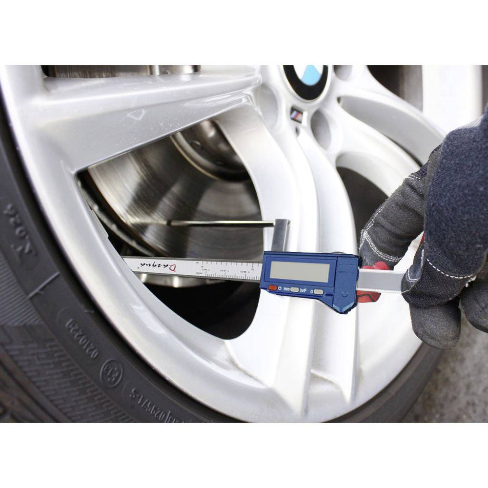 Hand mit Handschuh misst die Dicke einer Bremsscheibe an einem Autoreifen mit digitalem Messschieber zur Überprüfung des Verschleißes.