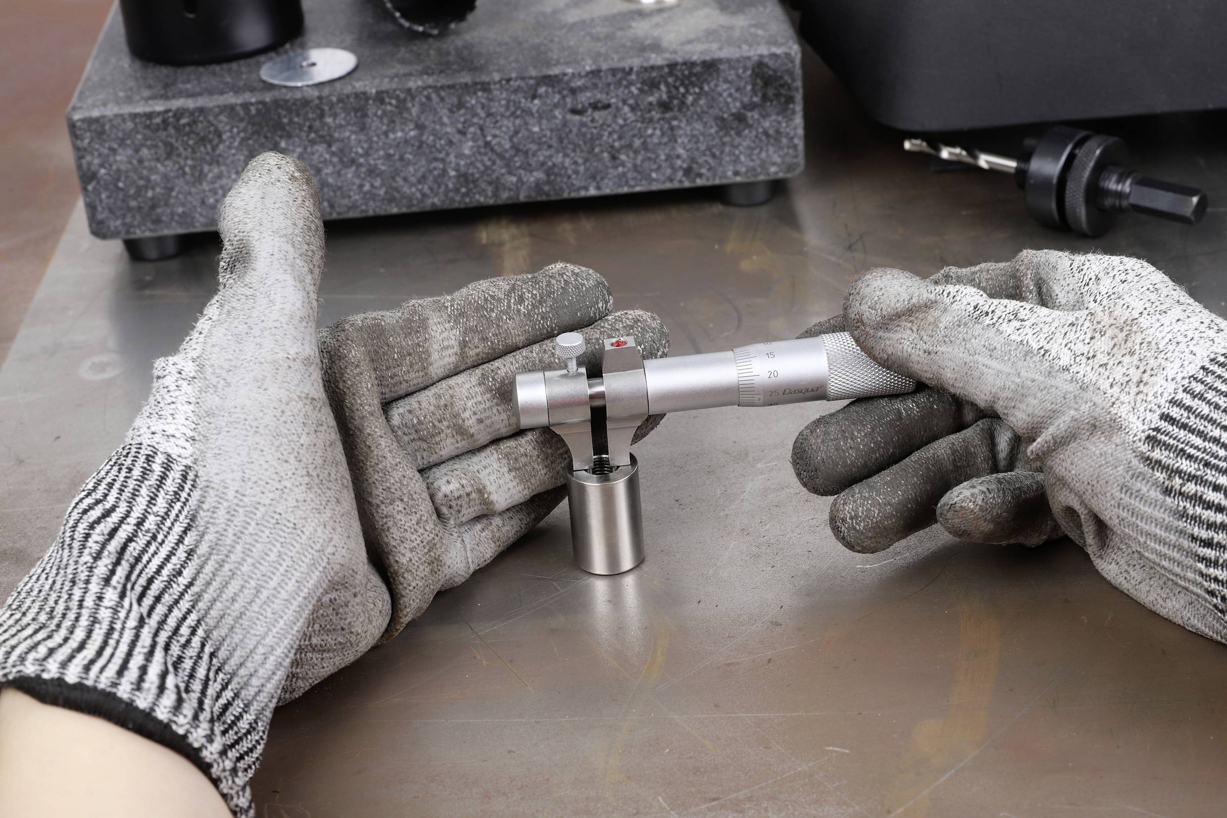 Person in Schutzhandschuhen benutzt ein Präzisionsmessgerät auf einer Metalloberfläche, um die Dicke eines Werkstücks zu messen.