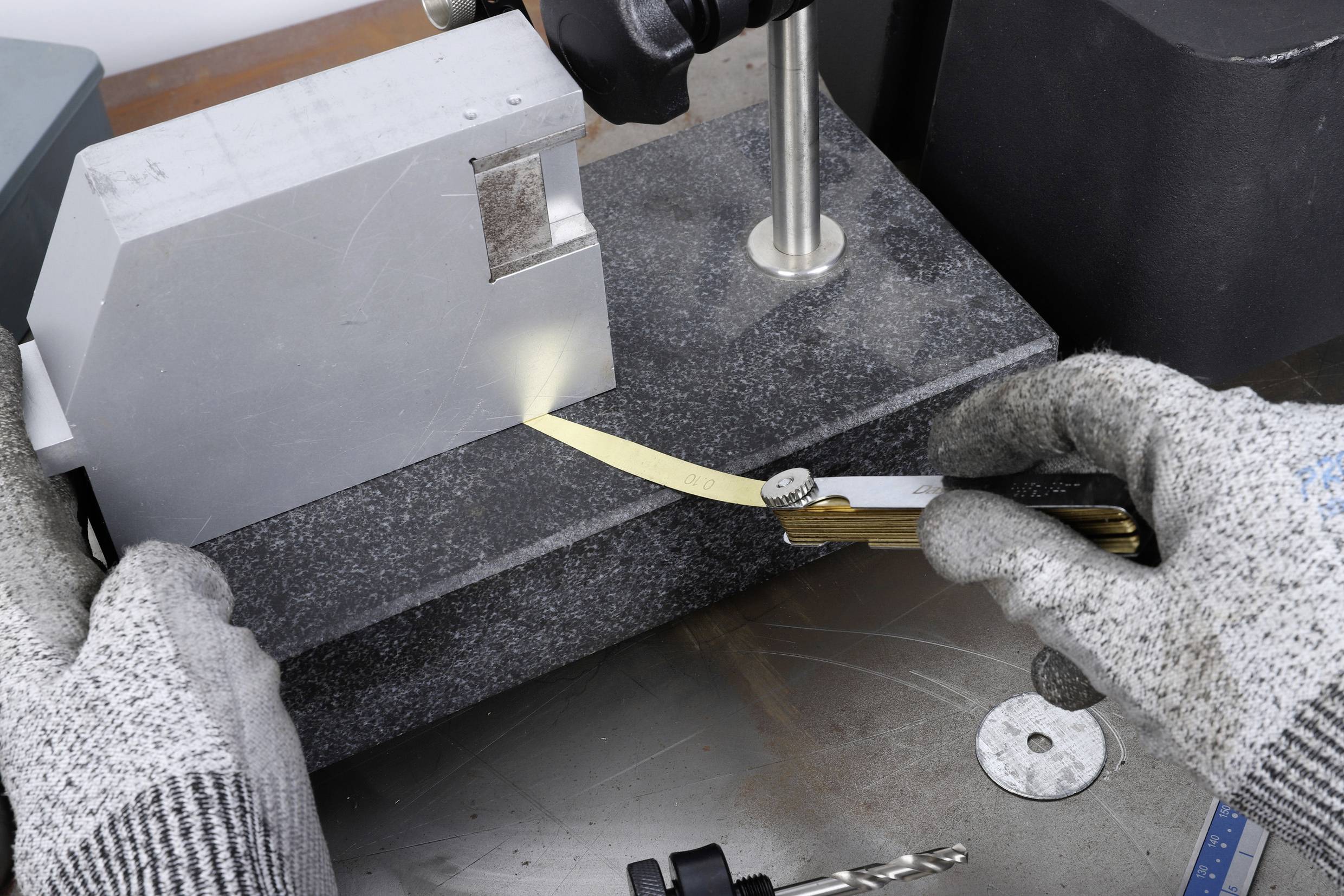 Eine Person prüft mit einem Messwerkzeug den Winkel eines metallischen Schneidewerkzeugs auf einem Granitmessblock.