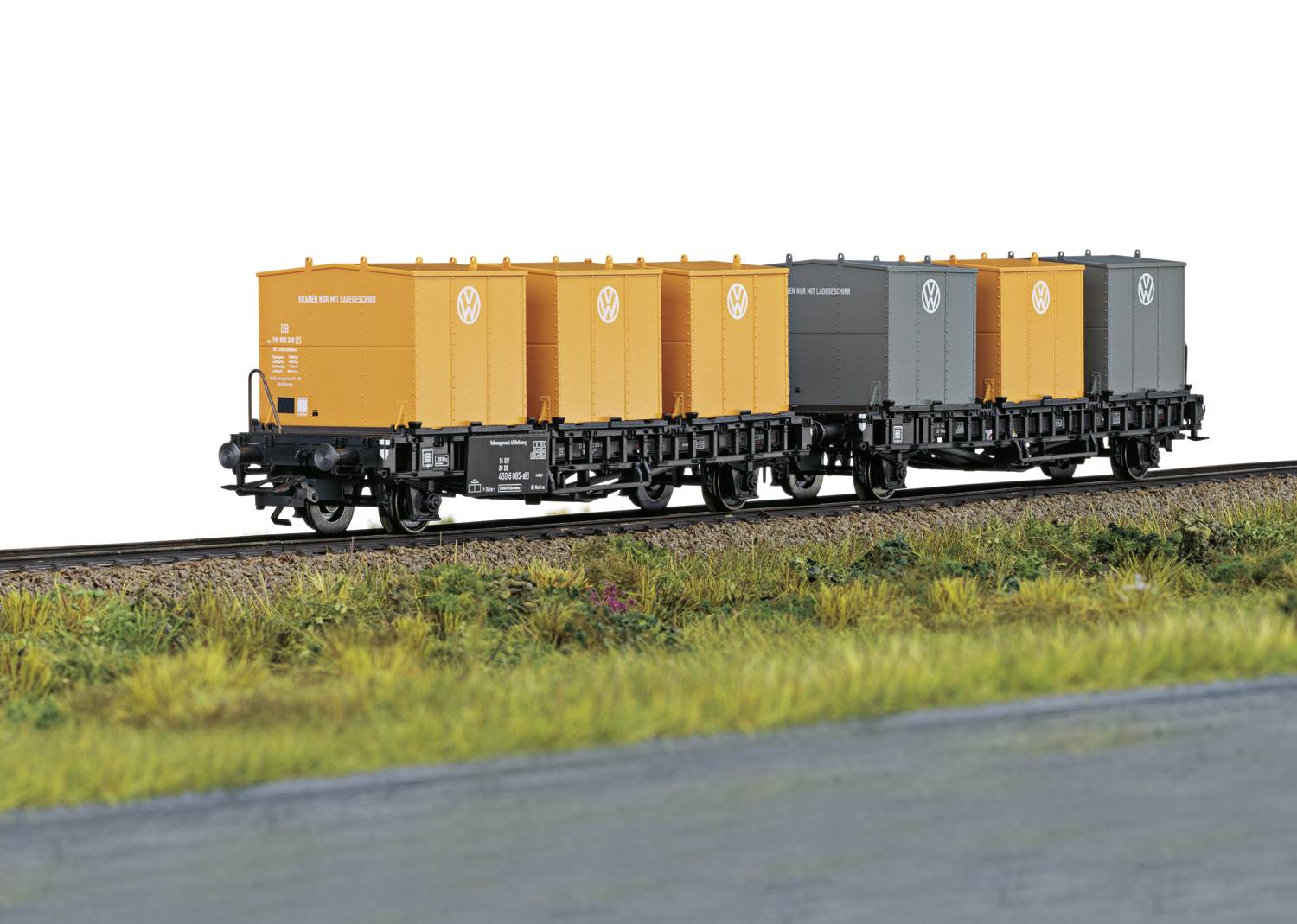 Ein Modelleisenbahn-Güterzug mit orangefarbenen und grauen Containern fährt auf einem Gleis durch eine grüne Landschaft.