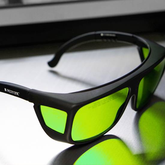 Eine schwarze 3D-Brille mit grünen Gläsern auf einem glatten, metallischen Untergrund liegend, fokussiert auf die Brille.