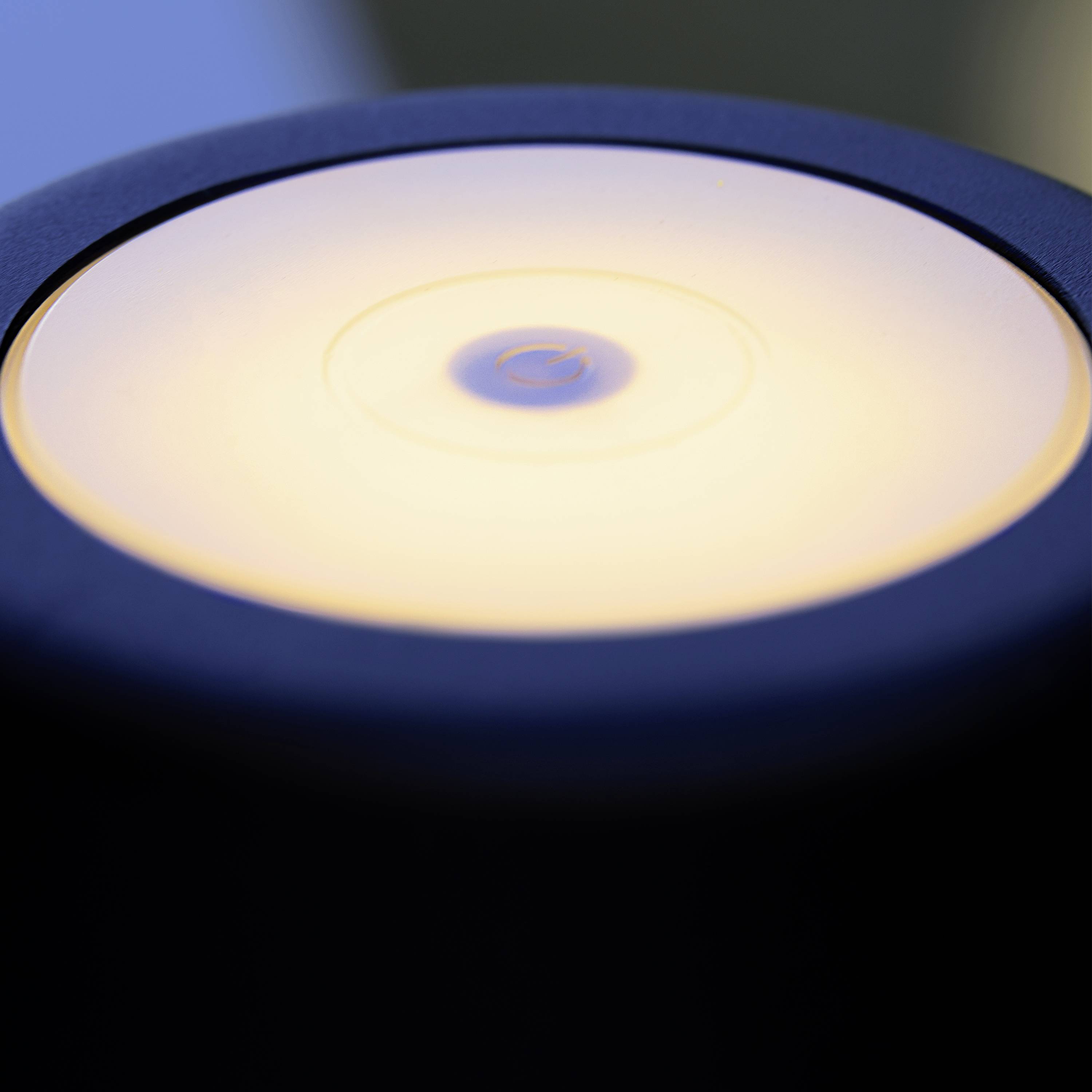 Eine Tischlampe mit kreisförmigem, leuchtendem Schirm, wahrscheinlich LED, in einem abgedunkelten Raum, schafft eine warme Atmosphäre.