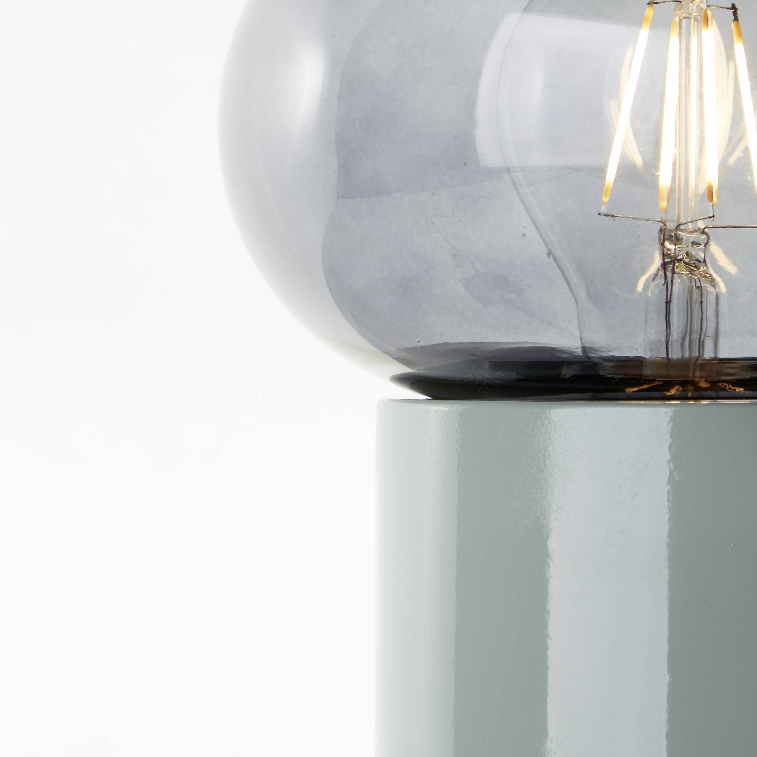 Ein hellgrauer, runder Lampenschirm aus Glas sitzt auf einer grauen Metallbasis. Die Glühbirne im Inneren ist sichtbar.