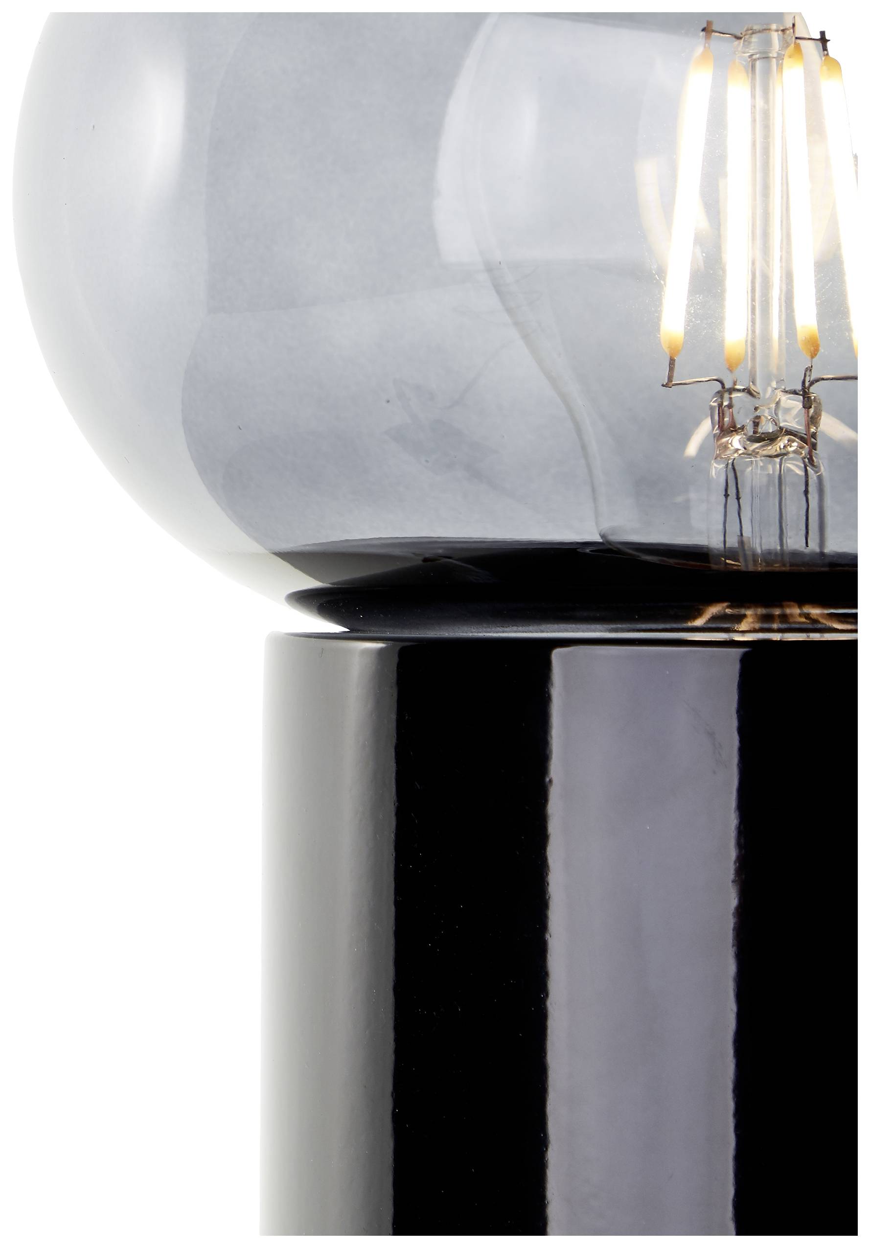 Nahaufnahme einer modernen Tischlampe mit schwarzem Sockel und Glasbirne, durch die leuchtende Glühfäden sichtbar sind.