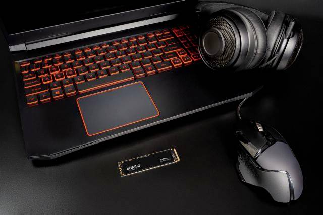 Ein Laptop mit beleuchteter Tastatur, Headset und Maus liegt auf einem Tisch. Ein SSD-Modul ist daneben sichtbar.