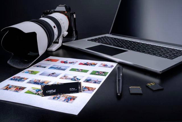Eine DSLR-Kamera, ein Laptop, ein USB-Stick, zwei Speicherkarten und ein Fotoblatt mit mehreren kleinen ausgedruckten Bildern auf einem Tisch.