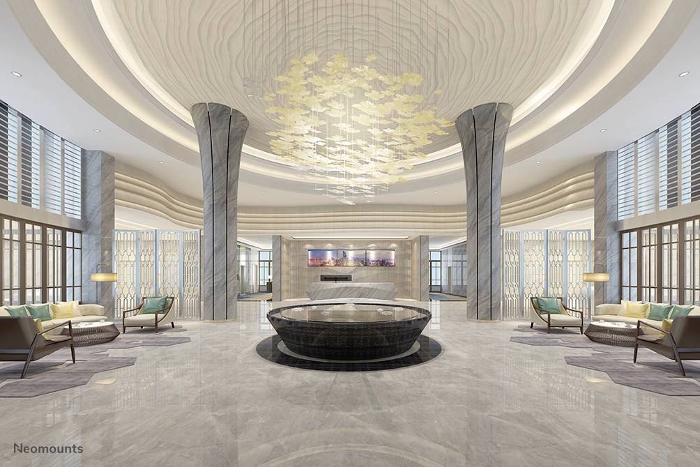 Geräumige Hotellobby mit zentralem, rundem Tisch, umgeben von modernen Sitzbereichen. Beeindruckendes Deckenleuchten-Design aus Metall.