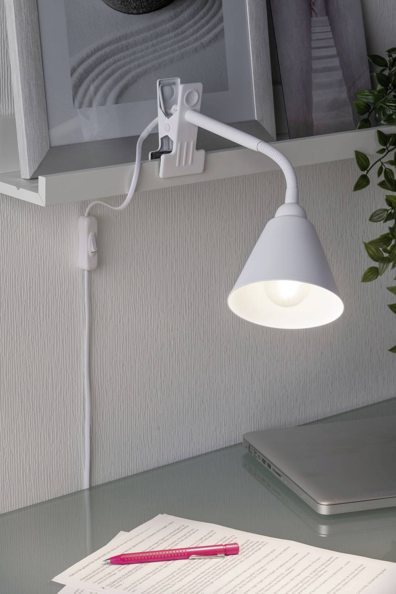 Weiße Schreibtischlampe leuchtet auf einen Tisch mit Dokumenten, rotem Stift und Laptop.