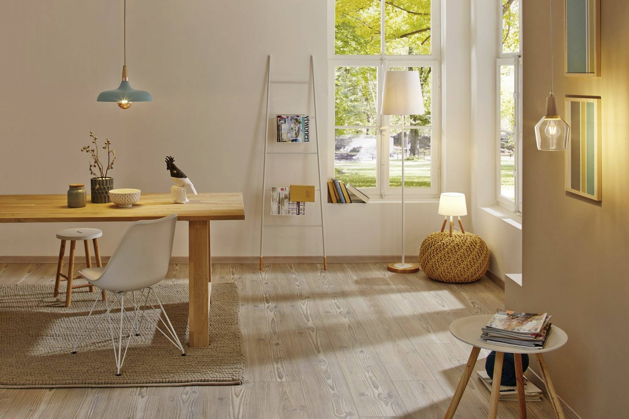 Ein minimalistisches Wohnzimmer mit Holztisch, weißem Stuhl und Regalen. Große Fenster lassen Tageslicht einfallen. Moderne Beleuchtung.