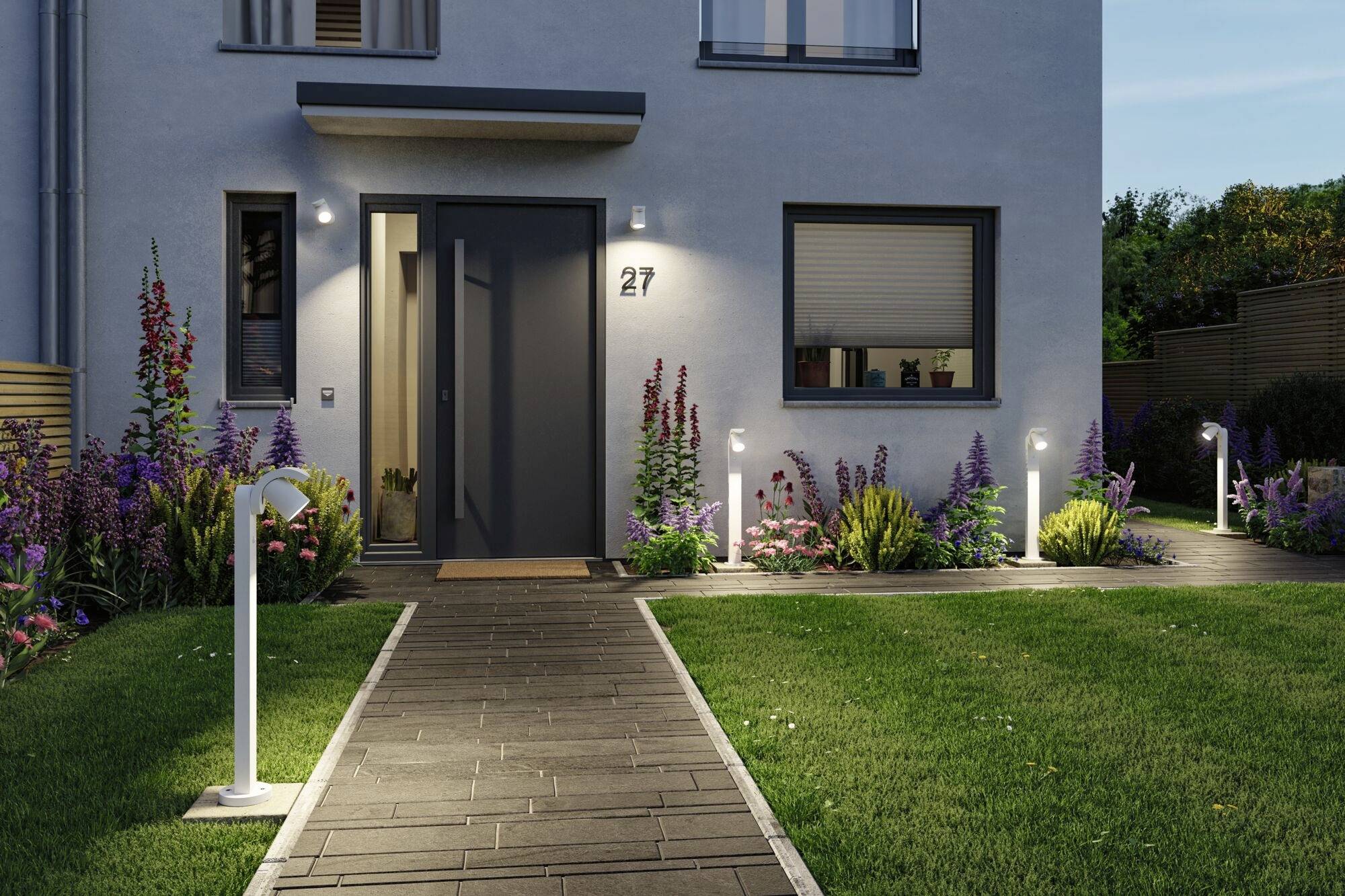 Ein modernes Haus mit grauer Fassade, beleuchtetem Eingang und umgeben von blühendem Garten und Gehweglichtern.