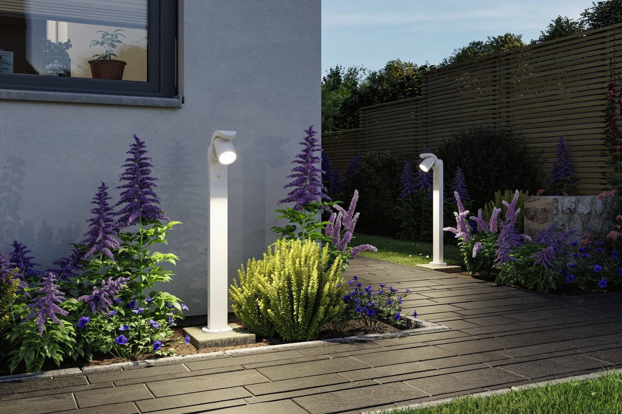 Gartenweg mit moderner Beleuchtung, umgeben von lila und grünen Pflanzen, neben einem Haus bei Dämmerung.