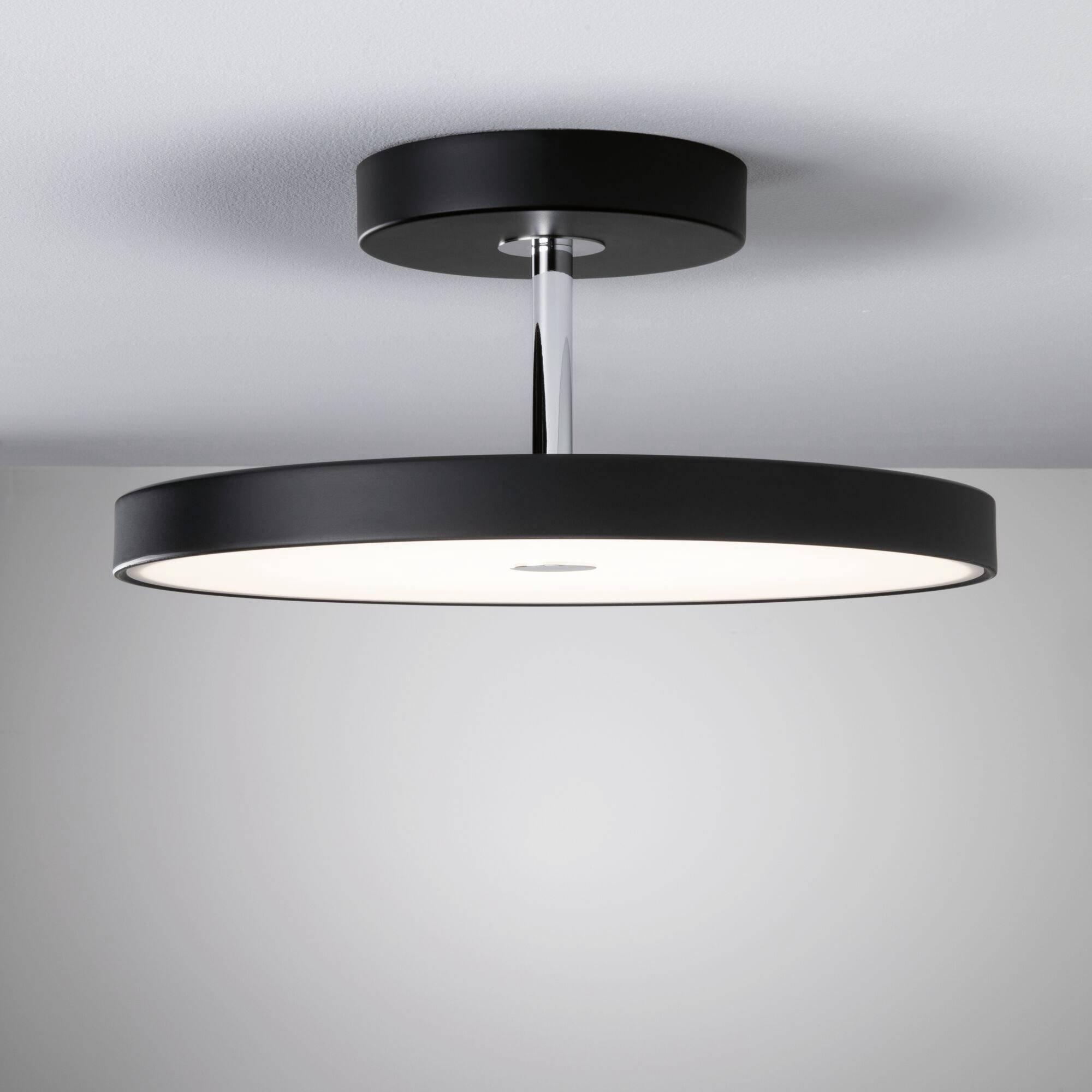 Schwarze, runde Deckenlampe mit modernem Design, leuchtet von der Decke herab, erzeugt gleichmäßiges, diffuses Licht im Raum.