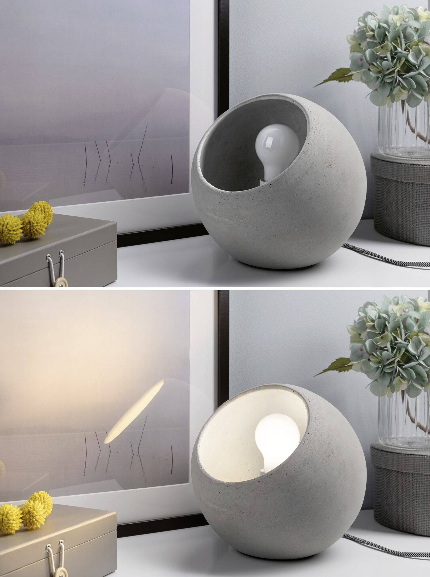 Zwei kugelförmige Lampen aus Beton auf einem Tisch, unterschiedlich platziert, mit Blumen und einem Bild im Hintergrund.