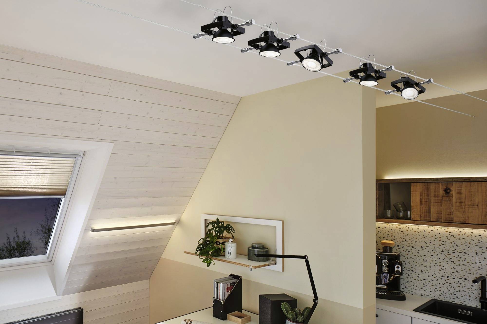 Eine moderne Küche mit schräger Holzdecke. Fünf Deckenstrahler beleuchten den Raum. Pflanzen und Dekor auf dem Regal an der Wand.