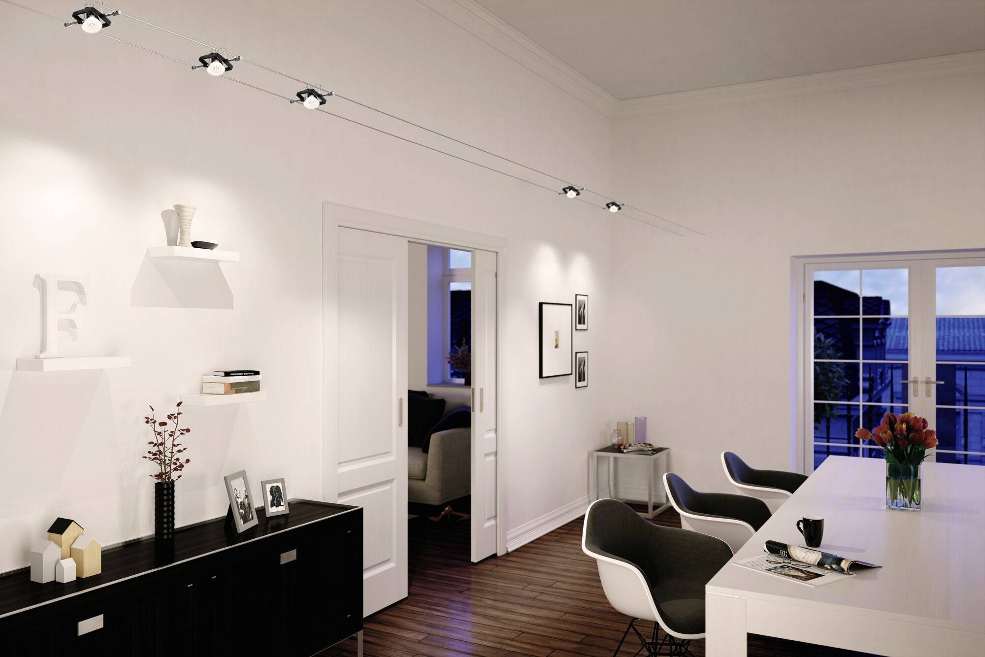Wohnzimmerinterieur mit weißem Tisch, modernen Stühlen und Regalen an der weißen Wand. Lampen beleuchten den Raum, Fensterblick nach draußen.