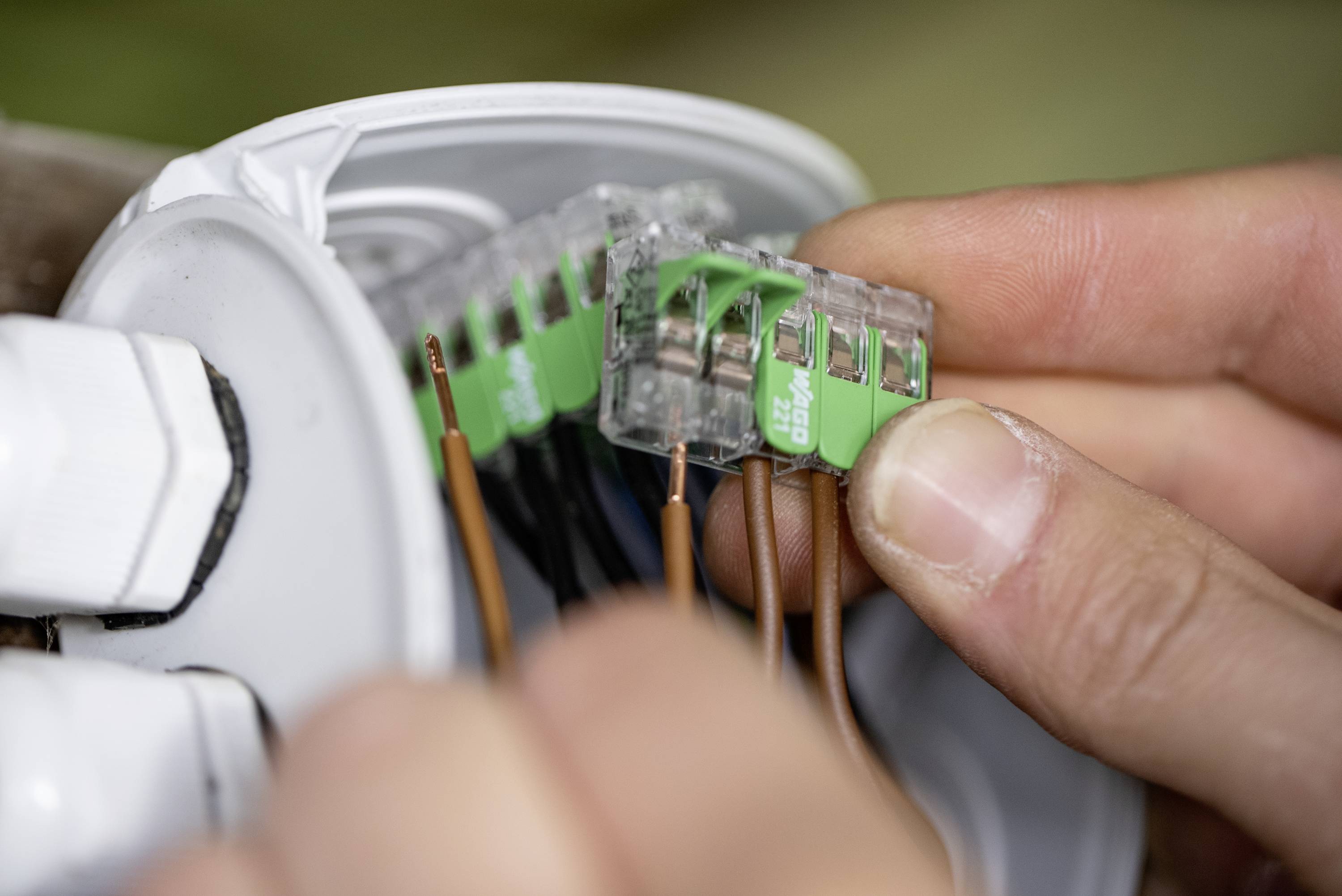 Eine Person verbindet mit den Händen mehrere elektrische Kabel im Inneren einer Anschlussdose.