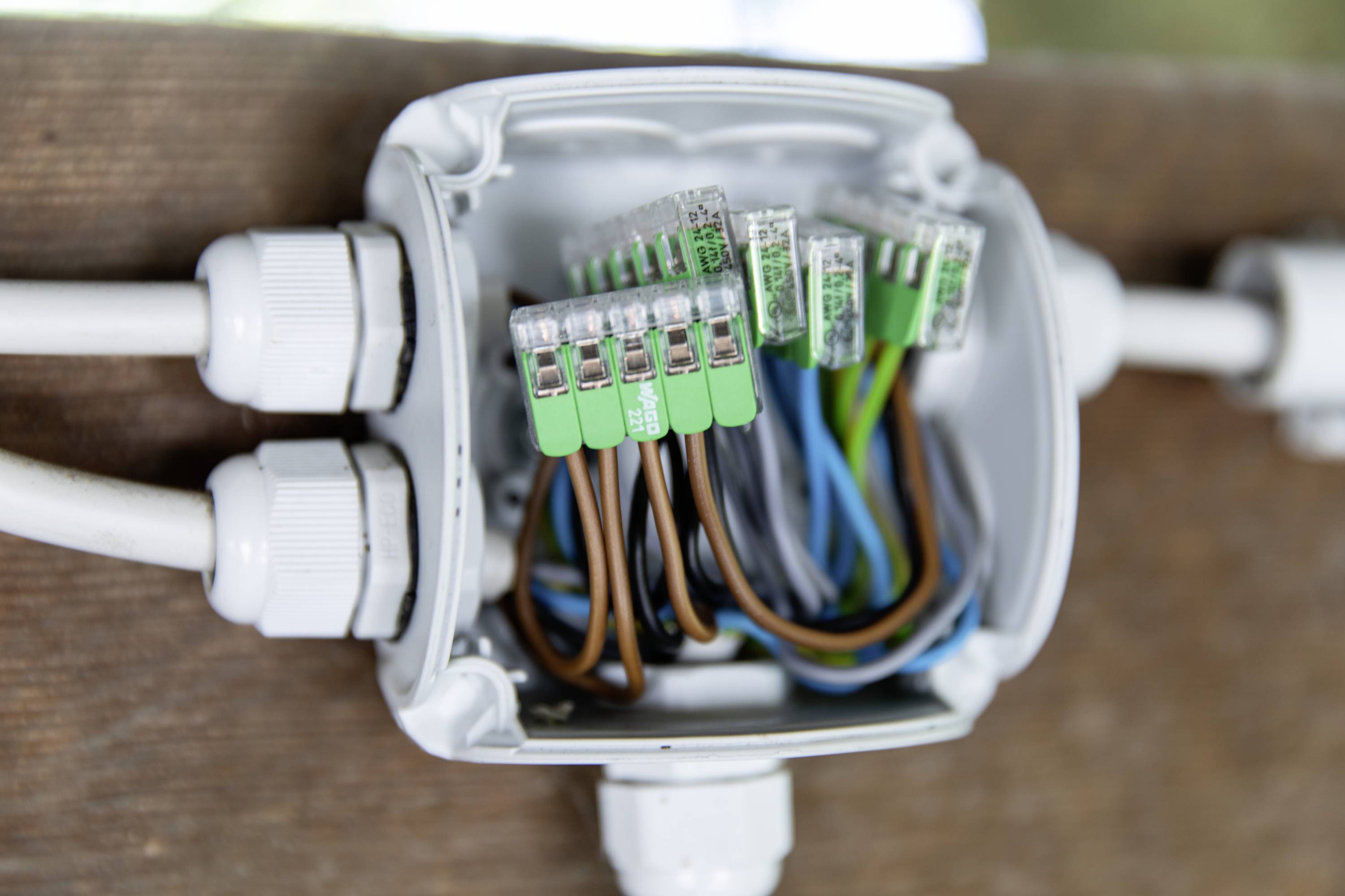 Eine geöffnete Verteilerdose mit verschiedenen farbigen Kabeln, die mit Klemmen befestigt sind, zeigt eine elektrische Verbindung.