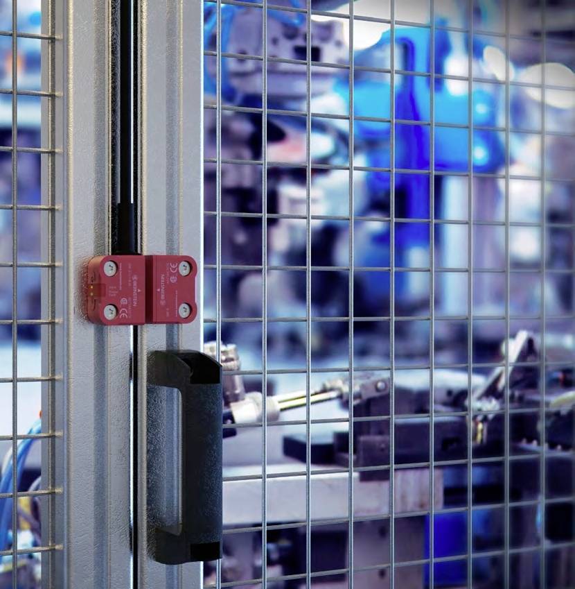 Ein roter Sicherheitsschalter ist an einem Maschendrahtzaun in einer Fabrikumgebung montiert, um Maschinenzugang zu sichern.