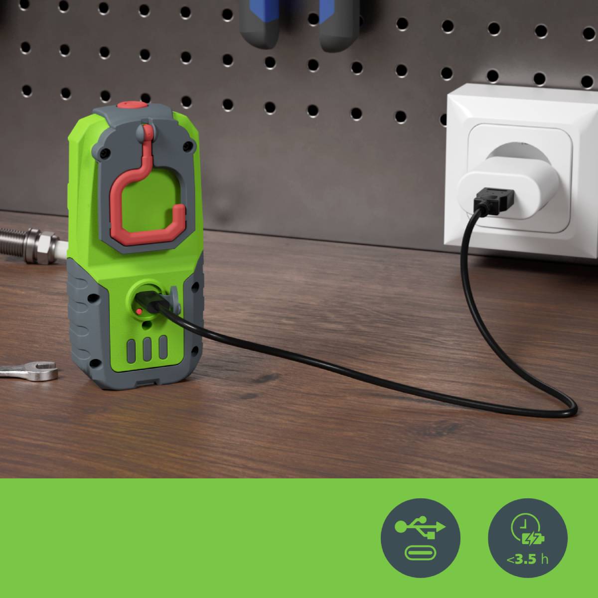 Ein grünes Ladegerät ist an eine Steckdose angeschlossen. Im Vordergrund liegt ein Schraubenschlüssel. Werkzeuge hängen im Hintergrund.
