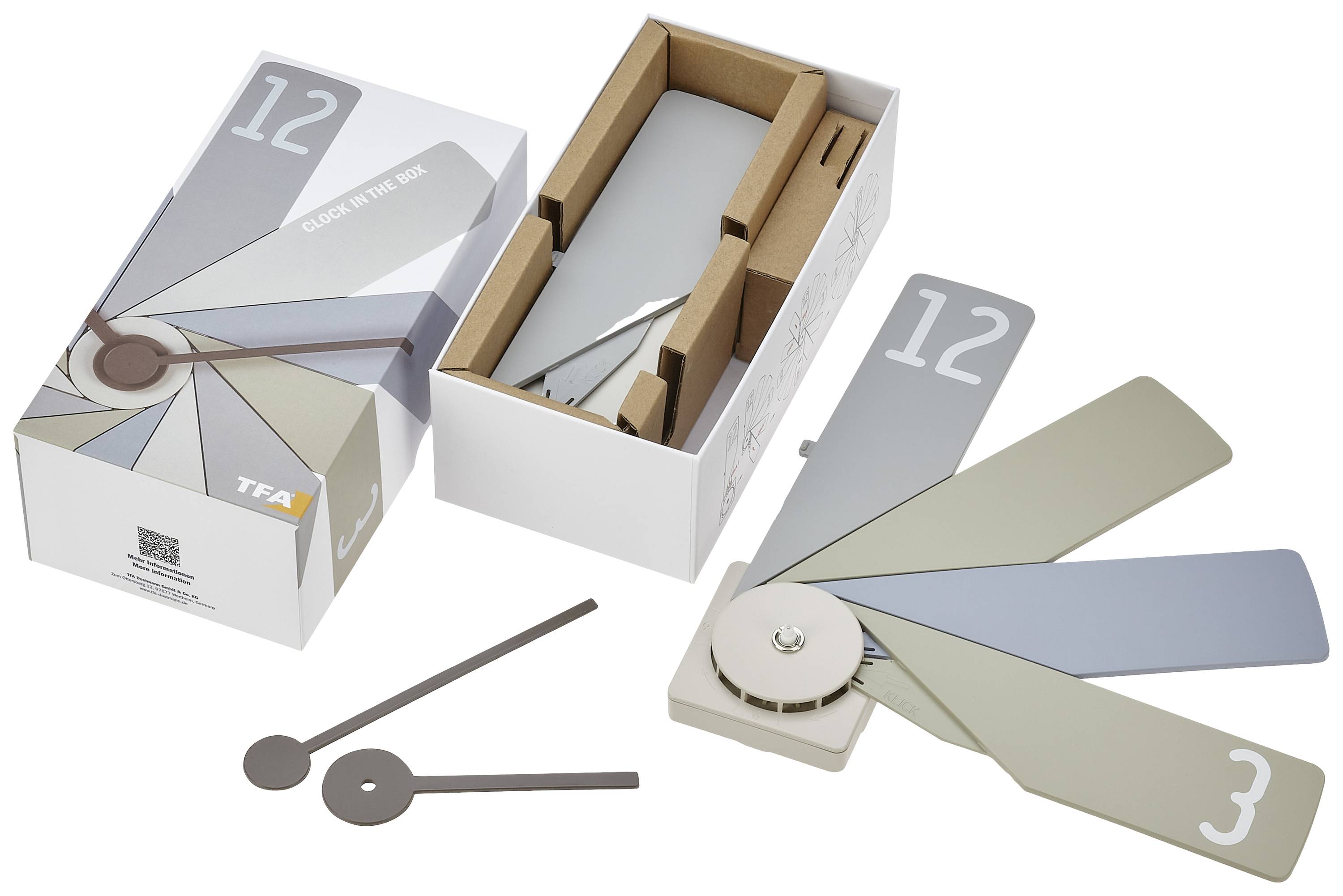 Verpackung einer Designeruhr aus Karton mit aufgeklapptem Rad und lackierten Platten in verschiedenen Grautönen, neben Zubehörteilen.
