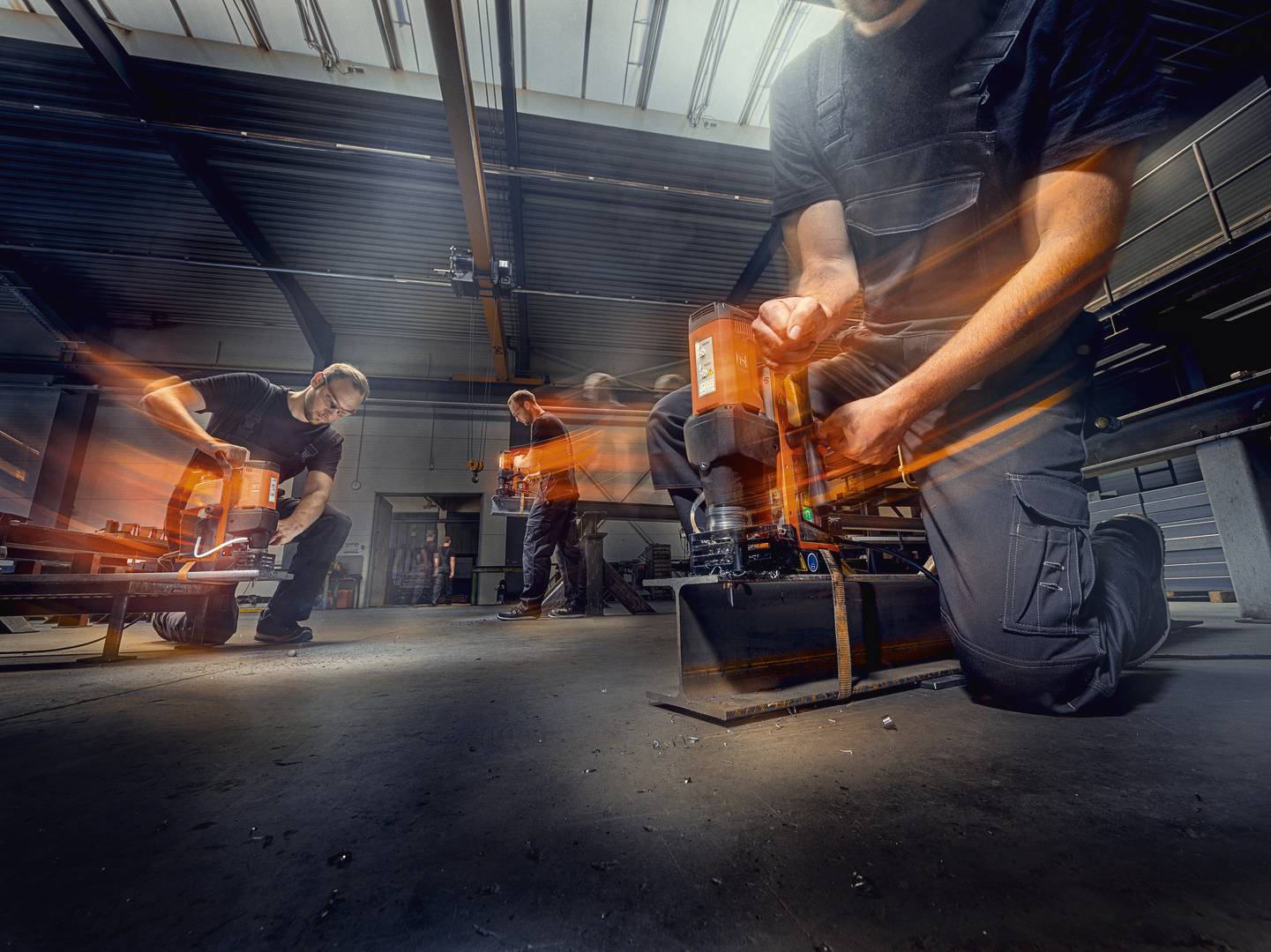 Arbeiter in einer Werkstatt verwenden orangefarbene Maschinen, Bewegungseffekte deuten auf aktive Arbeit und Geschwindigkeit hin.