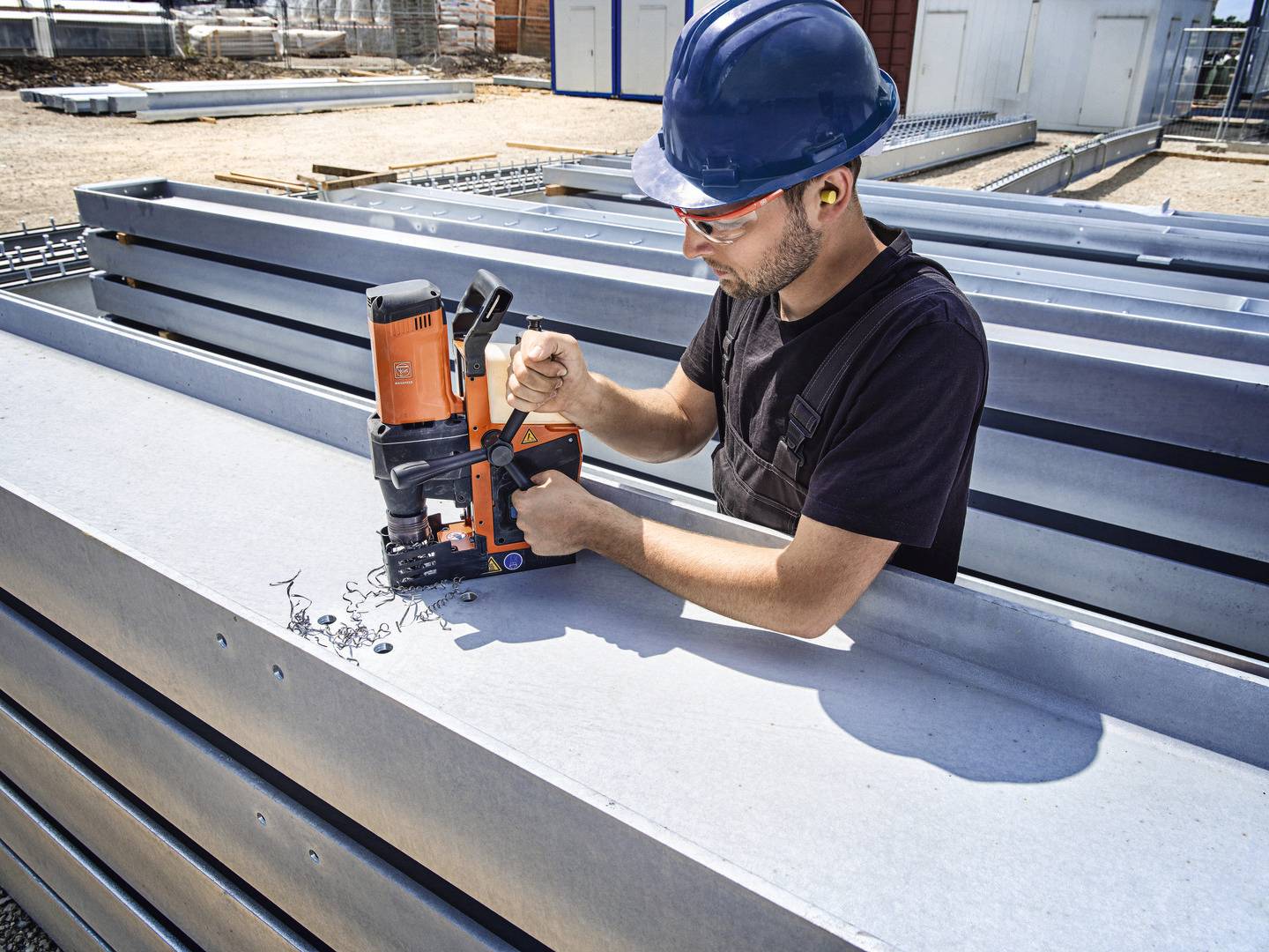 Arbeiter in Schutzkleidung bohrt mit einer Maschine ein Loch in einen Stahlträger auf einer Baustelle.