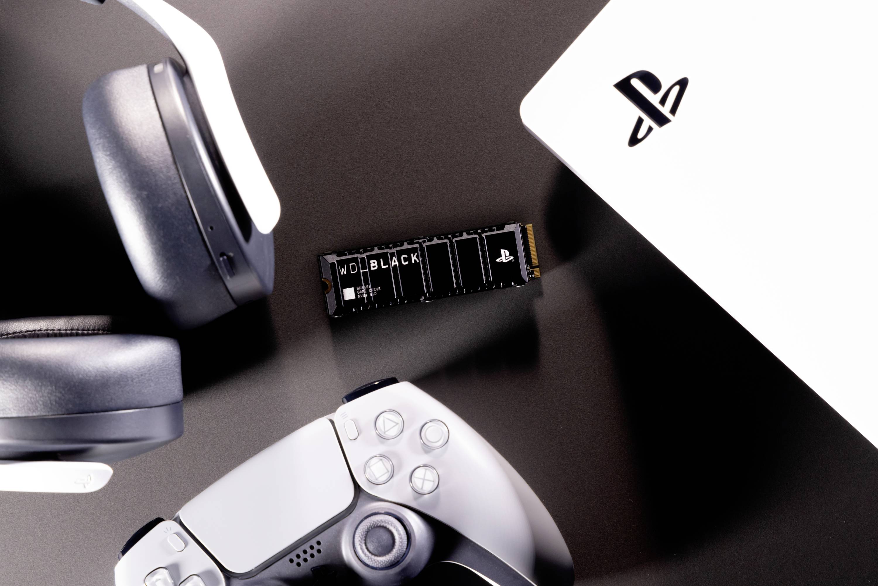 Ein Headset, ein Spielecontroller und eine SSD liegen auf einem Tisch neben einer Spielekonsole.