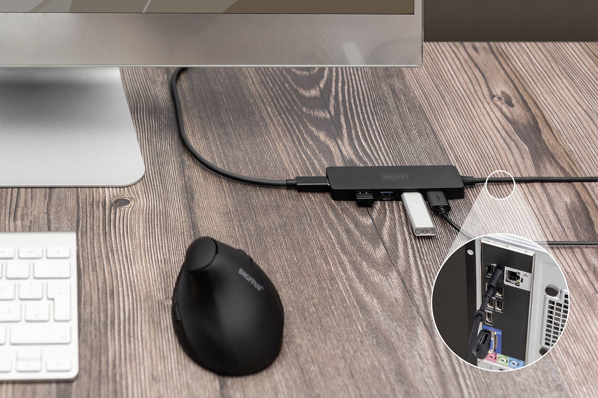 Monitor auf Holztisch, USB-Hub mit angeschlossenem Kabel, runder Ausschnitt zeigt PC-Rückseite mit Netzwerkanschluss und USB-Ports.