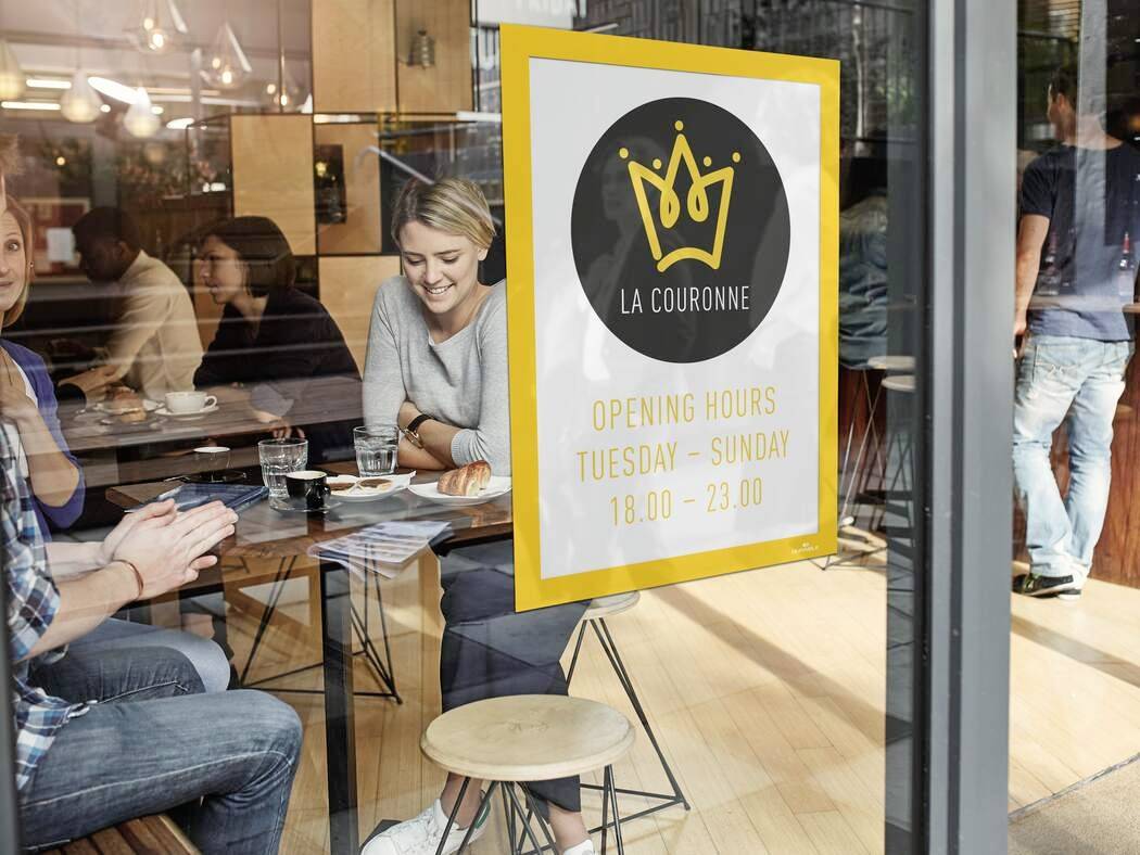 Eine Café-Szene mit Menschen am Tisch, draußen ein Schild mit einer goldenen Krone und 'La Couronne'. Öffnungszeiten: Dienstag-Sonntag, 18:00-23:00.