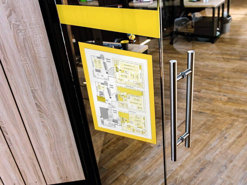 Fluchtplan auf Glastür im Büro, zeigt Gebäudegrundriss mit Rettungswegen, markiert in Gelb. Sicherheitsanweisung für Notfälle.