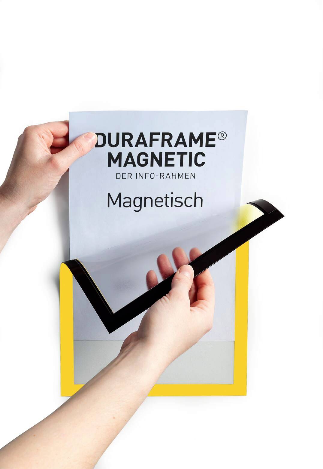 Hände halten ein gelbes magnetisches Rahmenmodell namens 'Duraframe Magnetic', während eine bedruckte Folie eingelegt wird.