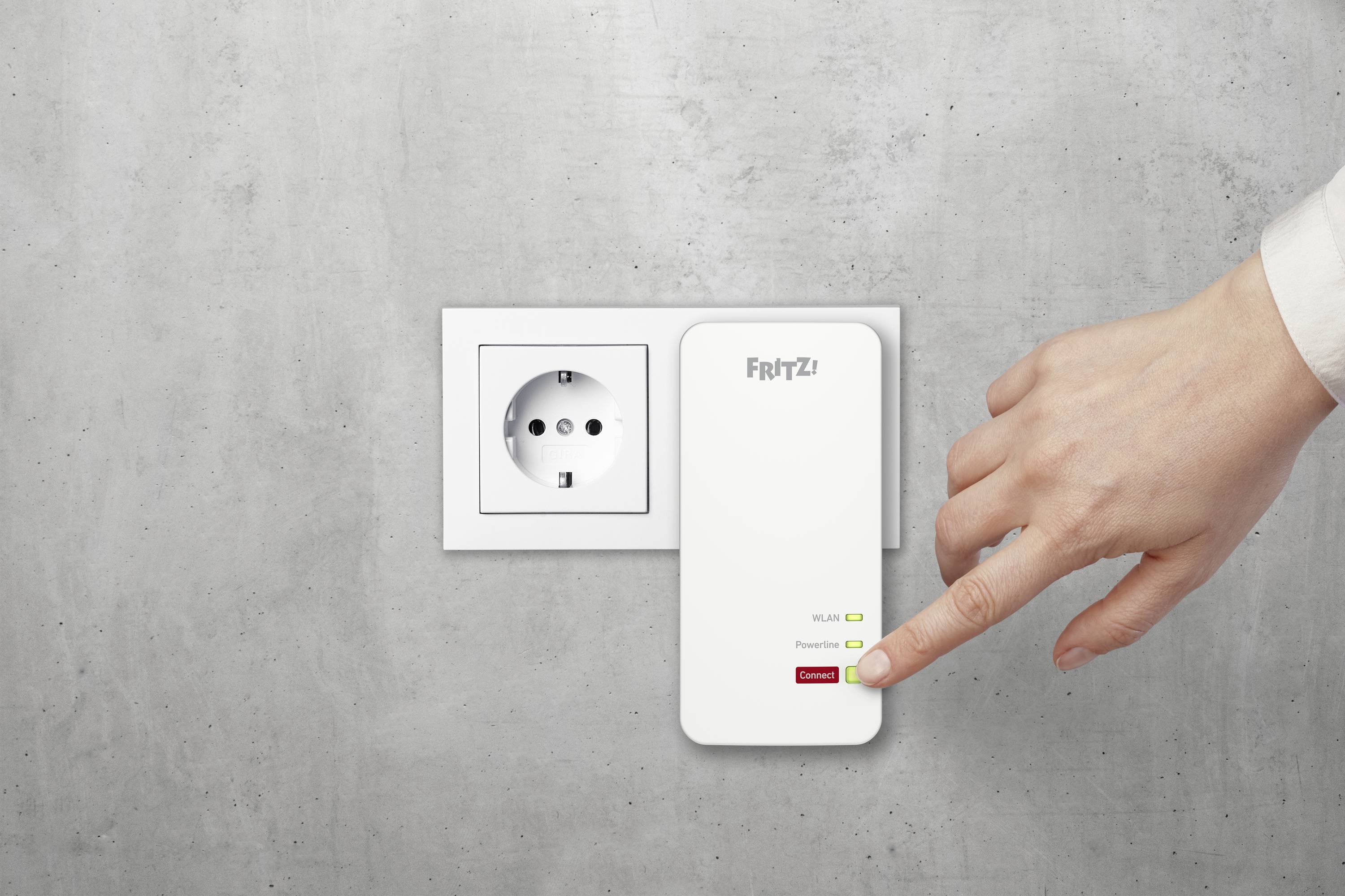 Eine Hand verbindet einen Wi-Fi-Repeater der Marke FRITZ! an eine Steckdose an einer grauen Wand.